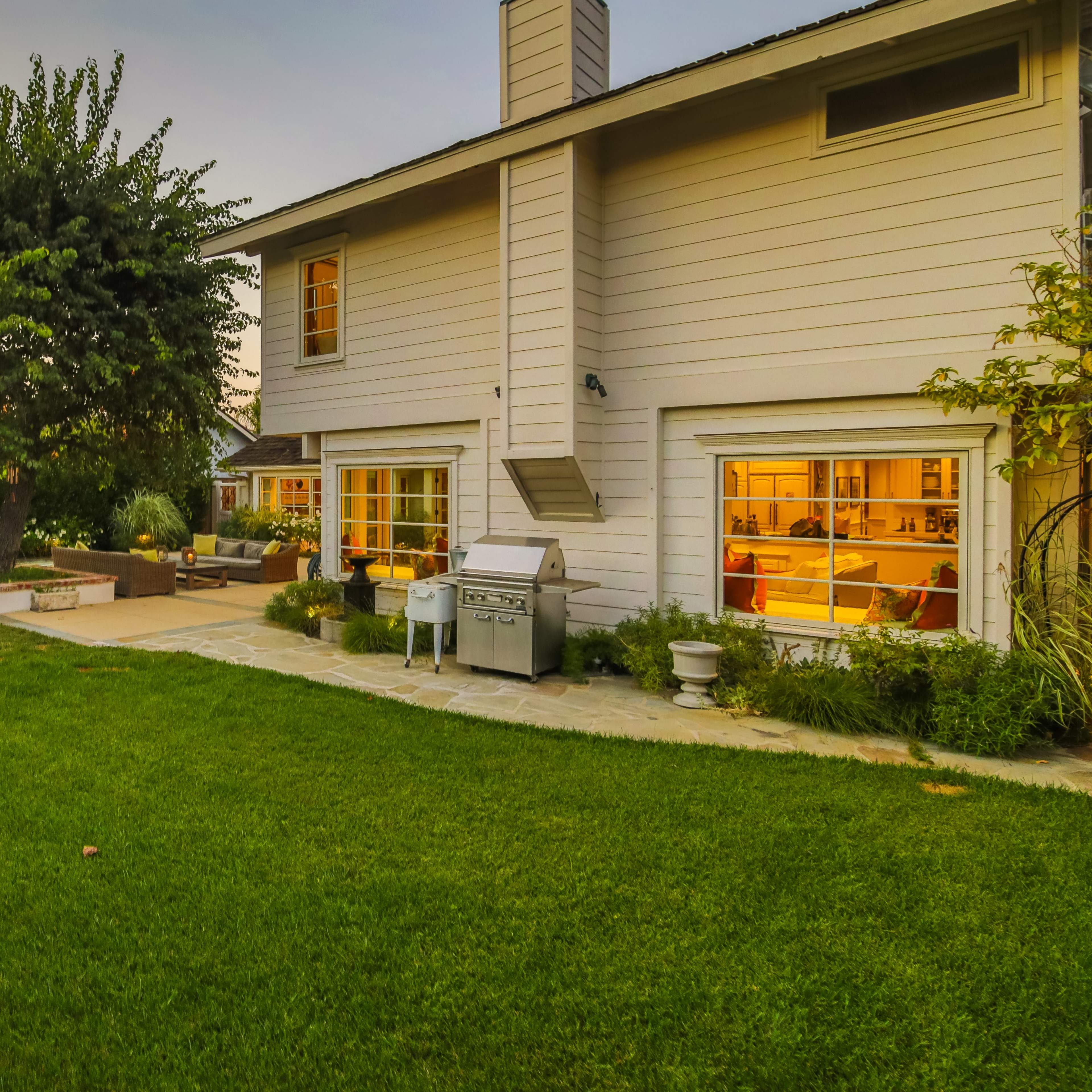 A backyard with a well-maintained lawn, a patio area, a barbecue grill, and several lounge chairs set near a fire pit.