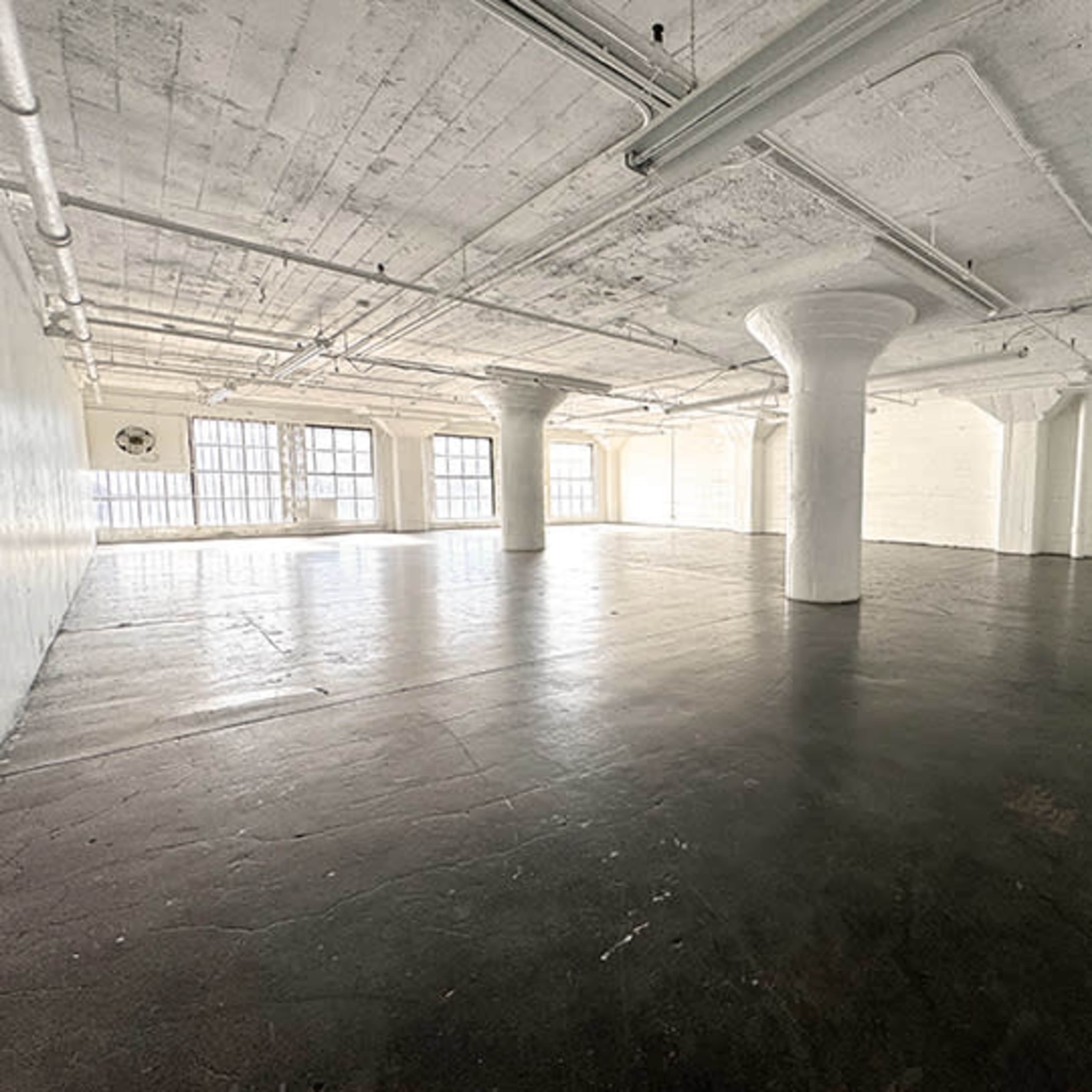 A large, empty industrial space with concrete flooring and tall windows.
