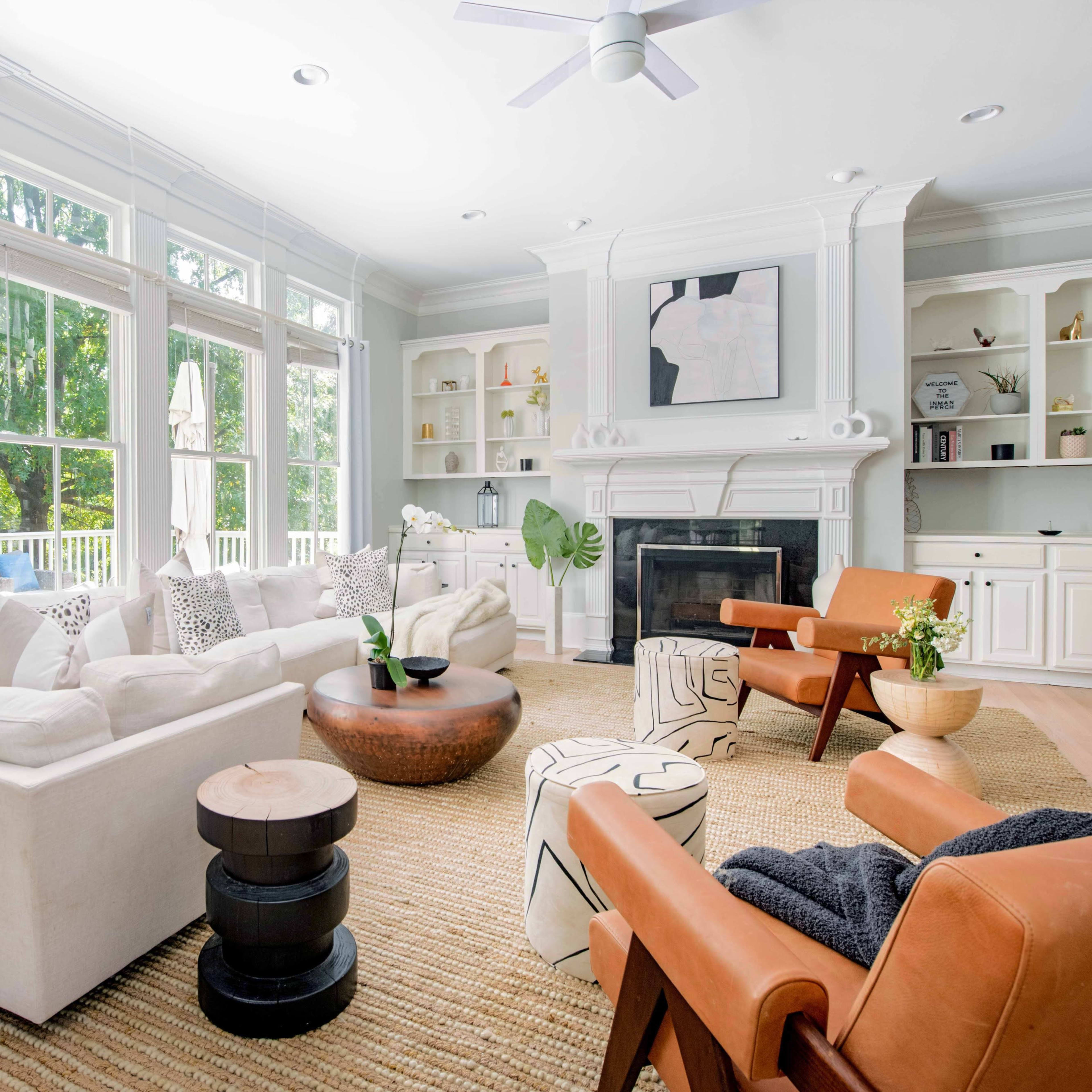 The living room features a large white sectional sofa, a round coffee table, and two armchairs, with large windows that provide ample natural light and a view of the outdoors.