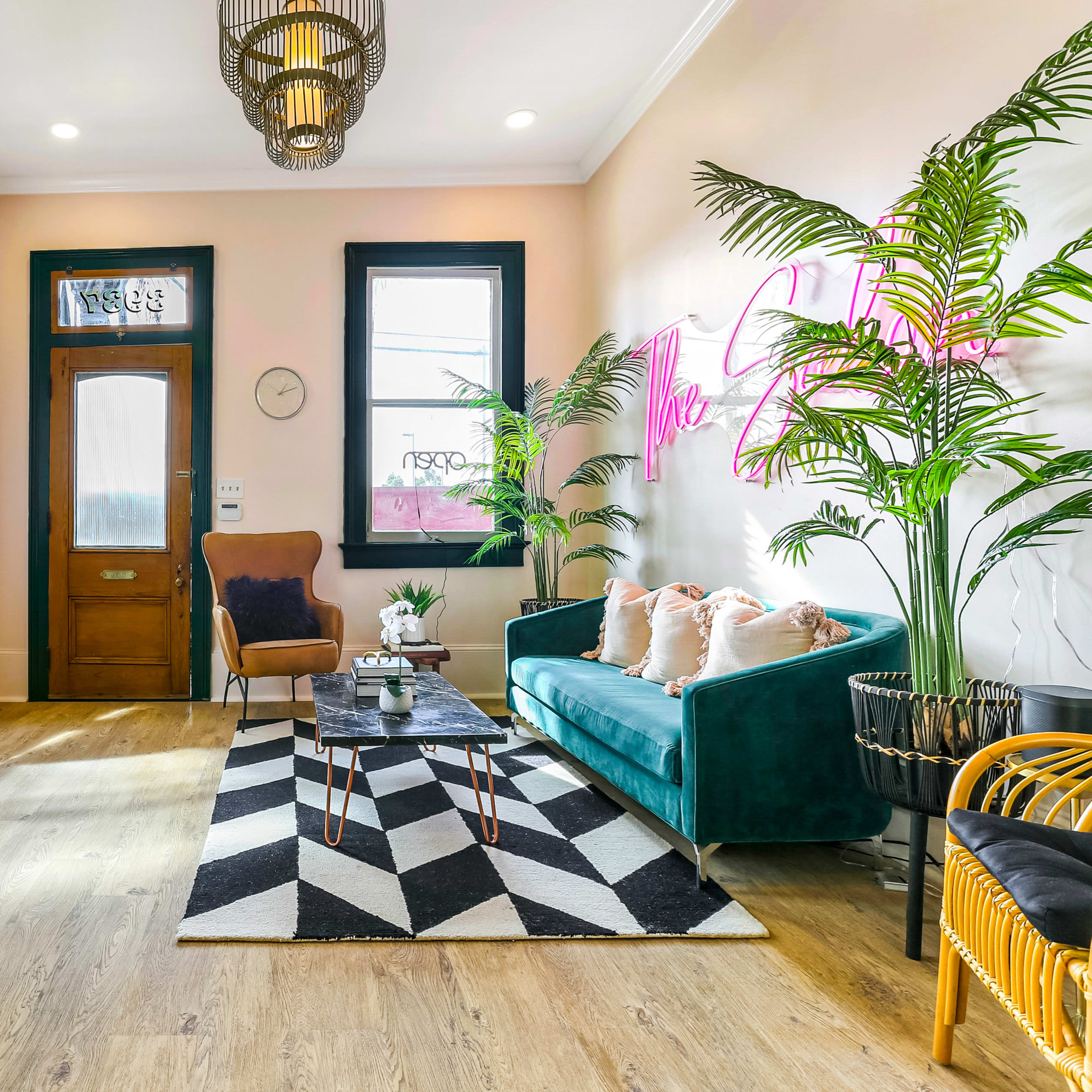 A brightly lit room featuring a teal sofa, a geometric black-and-white rug, plants, and decorative items arranged around a central coffee table.