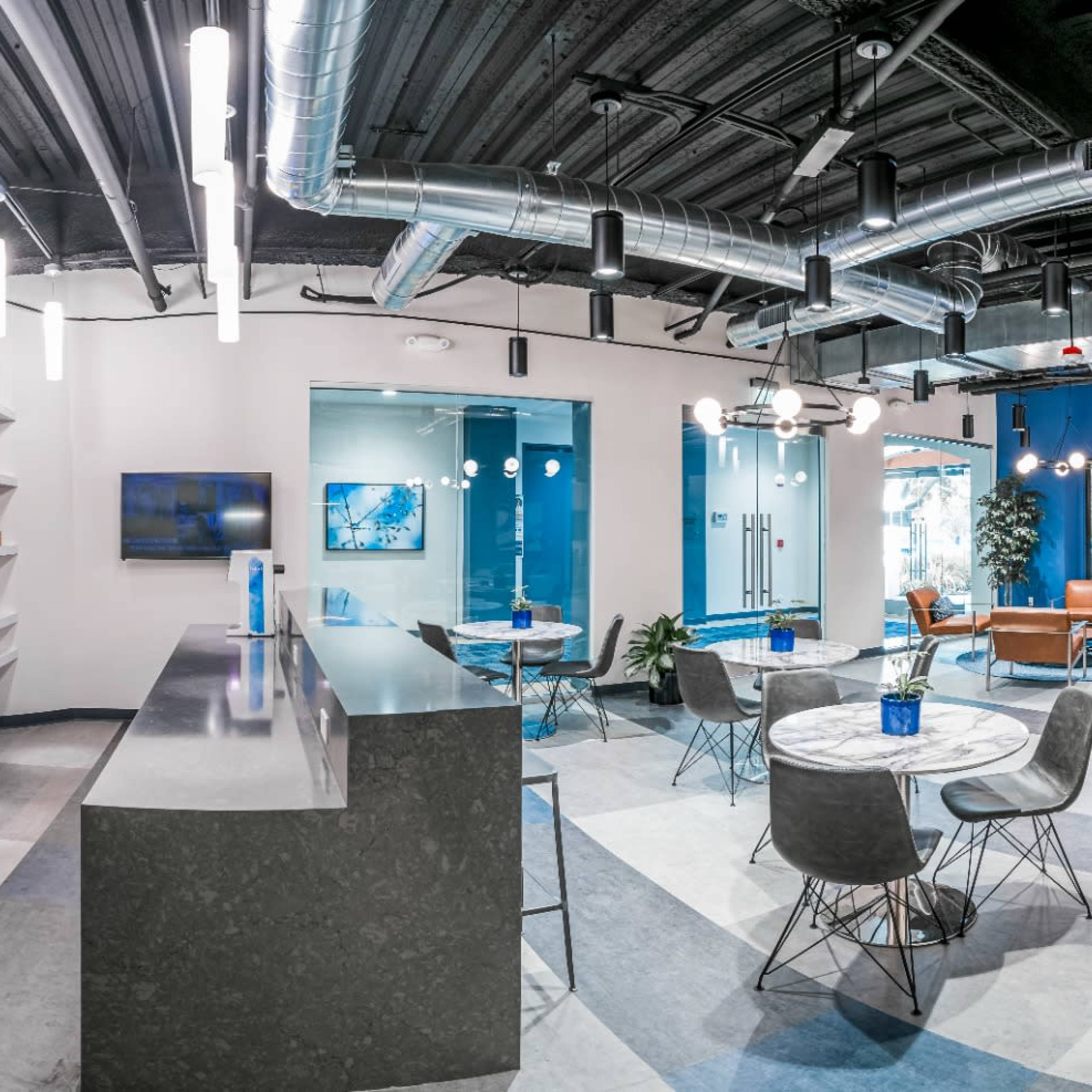 A modern office space with distinct areas for collaboration, including seating, a kitchen, and meeting rooms, divided by glass walls.