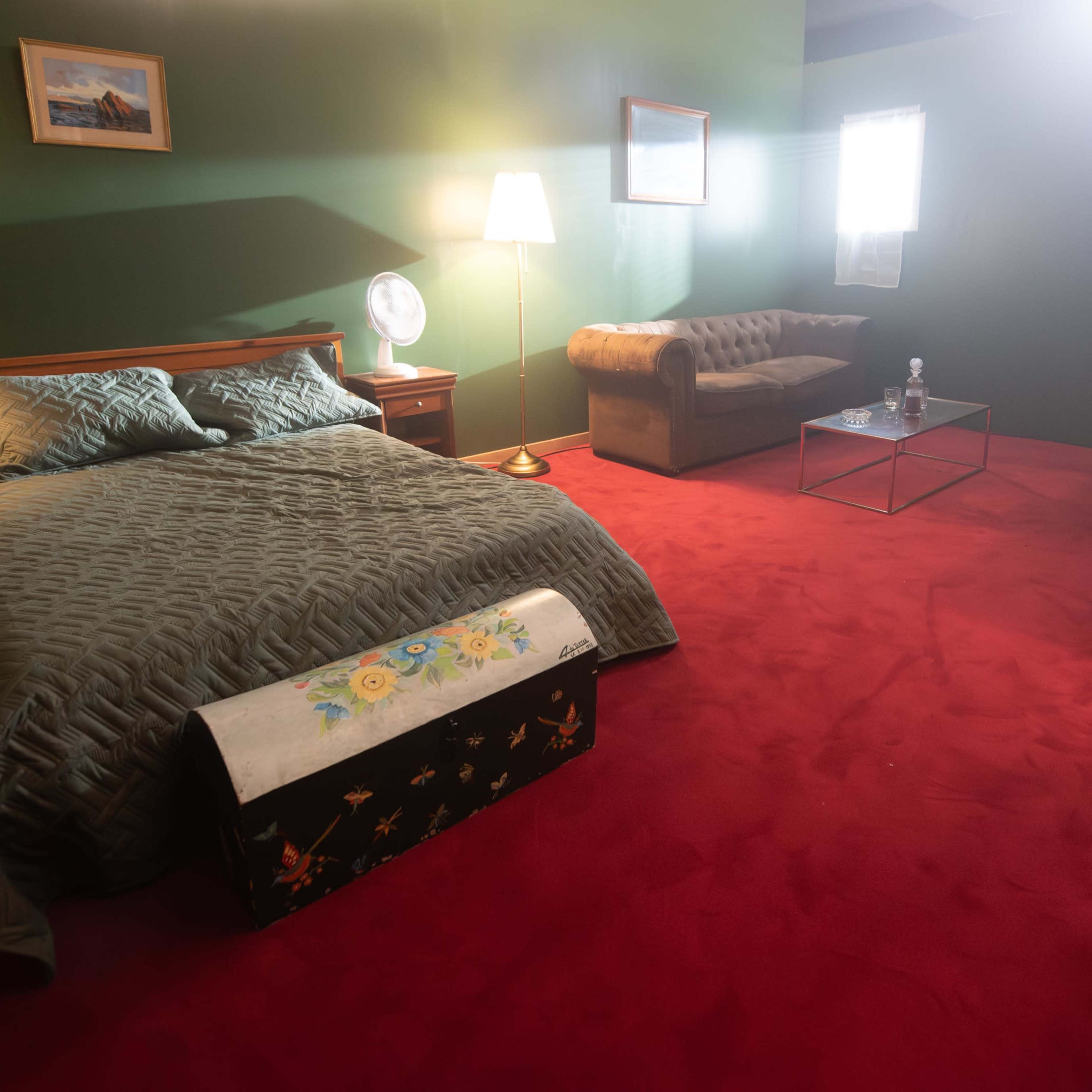 A bedroom with a large bed, a sofa, and a desk, all situated on a red carpet with green walls.