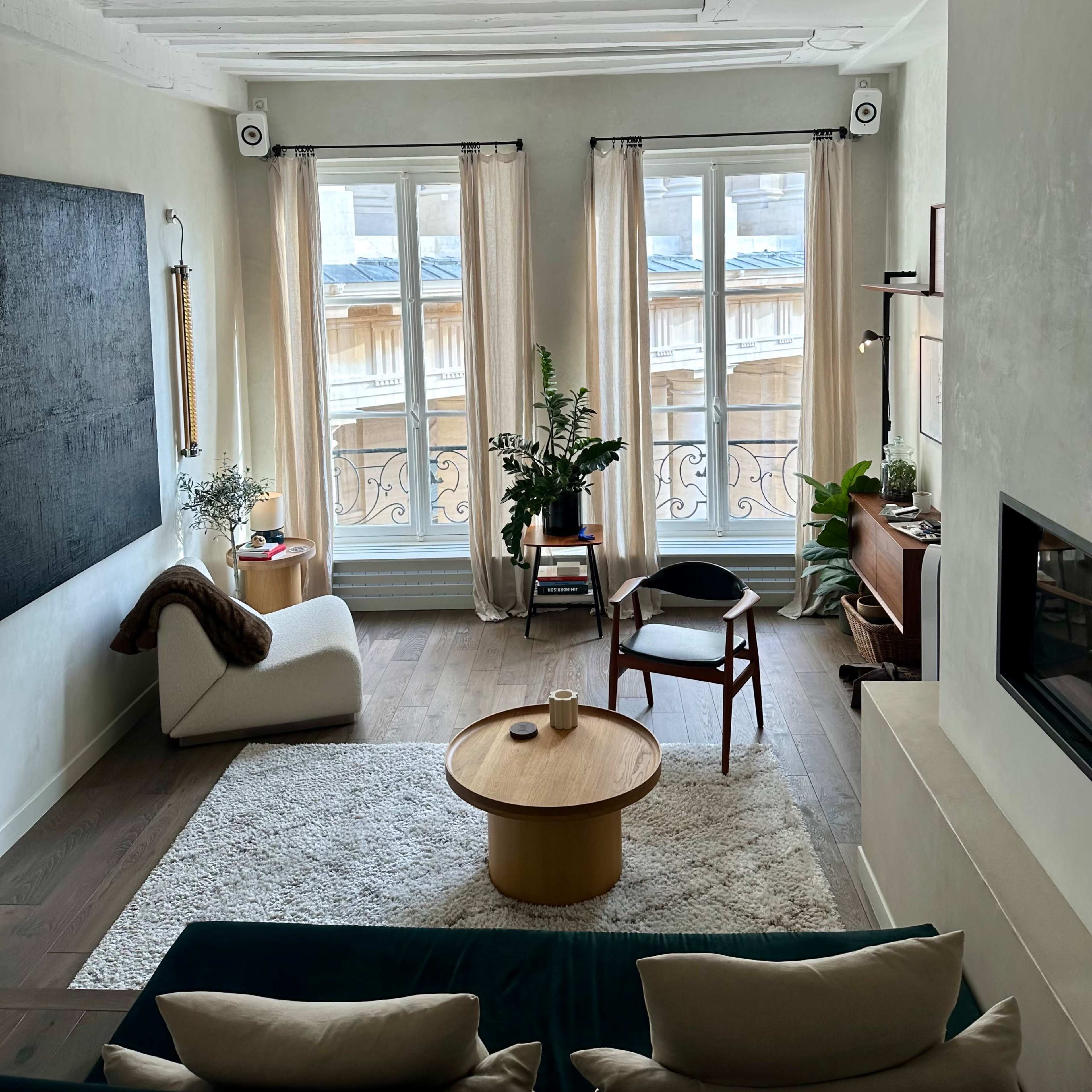 A well-furnished living room with large windows, a light rug, a round wooden coffee table, and a cozy seating area.