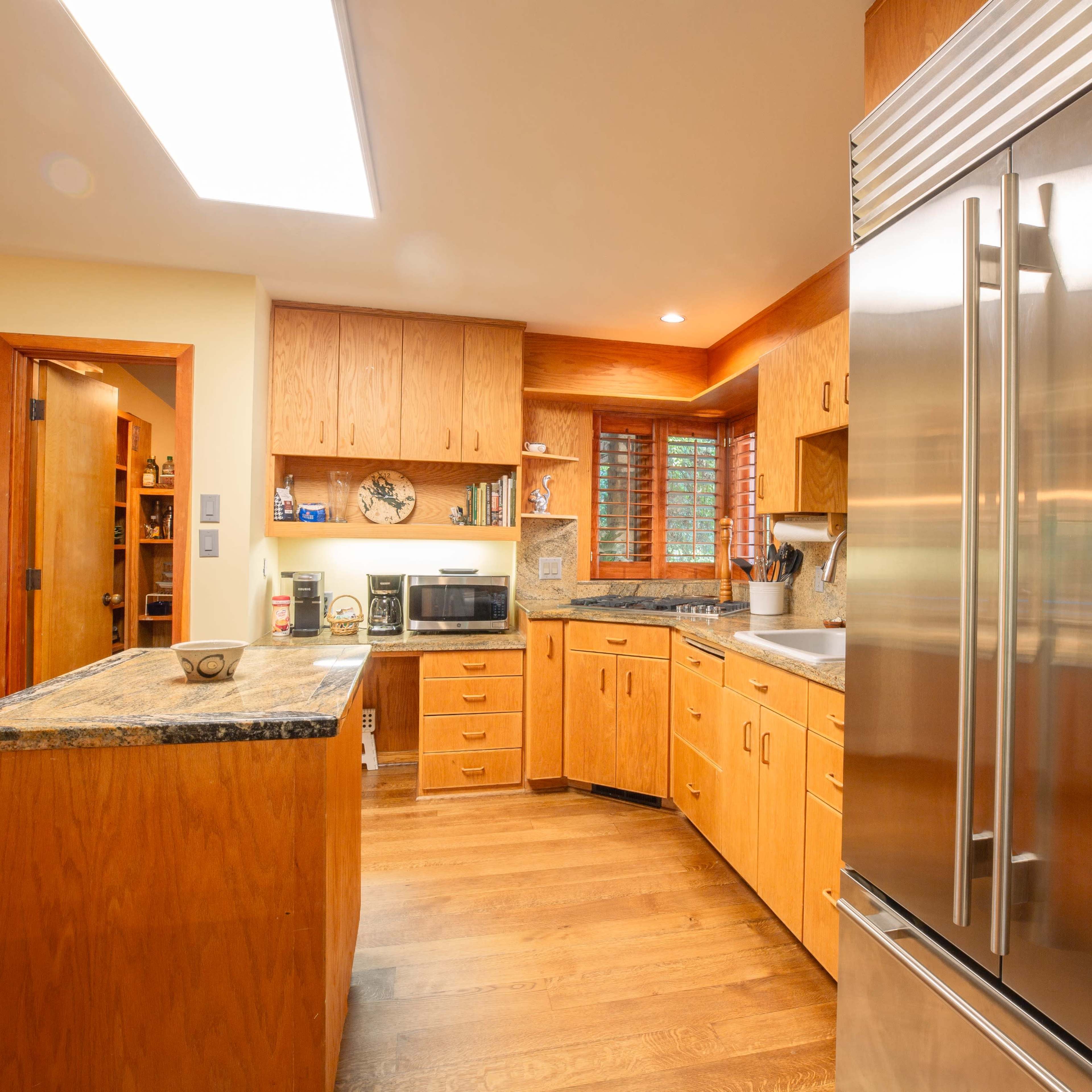 A modern kitchen featuring wooden cabinets, a large stainless steel refrigerator, and a granite countertop.