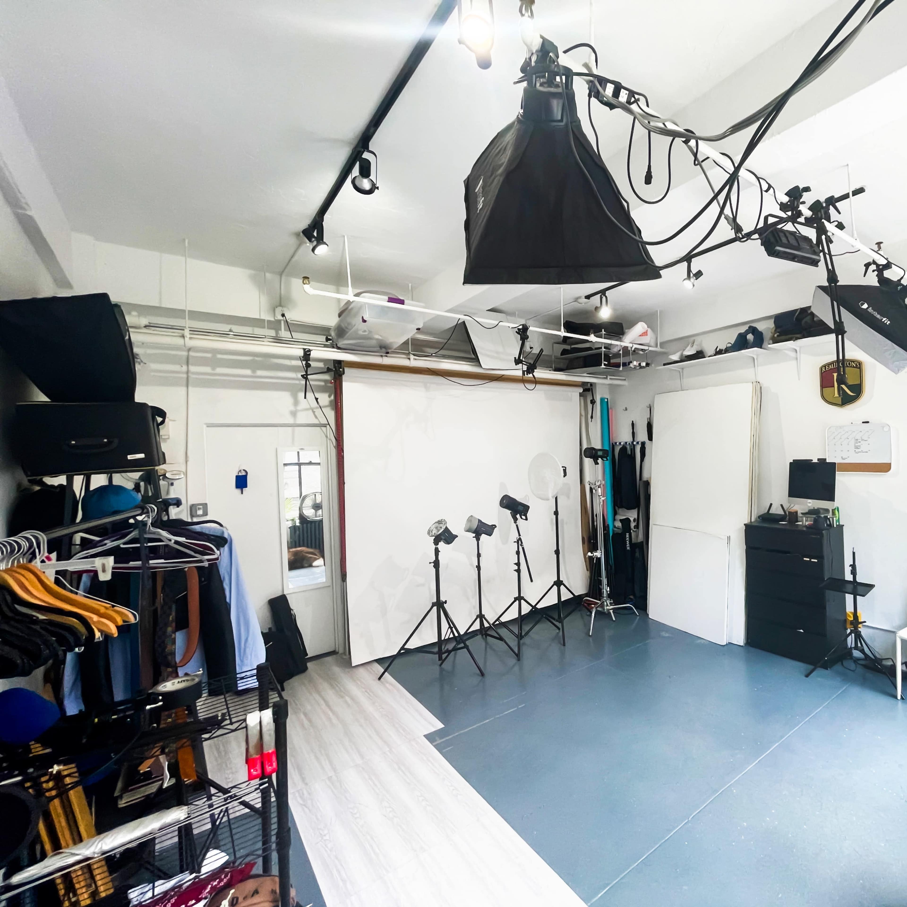 A photography studio with several lighting setups, clothing racks, and a white backdrop.