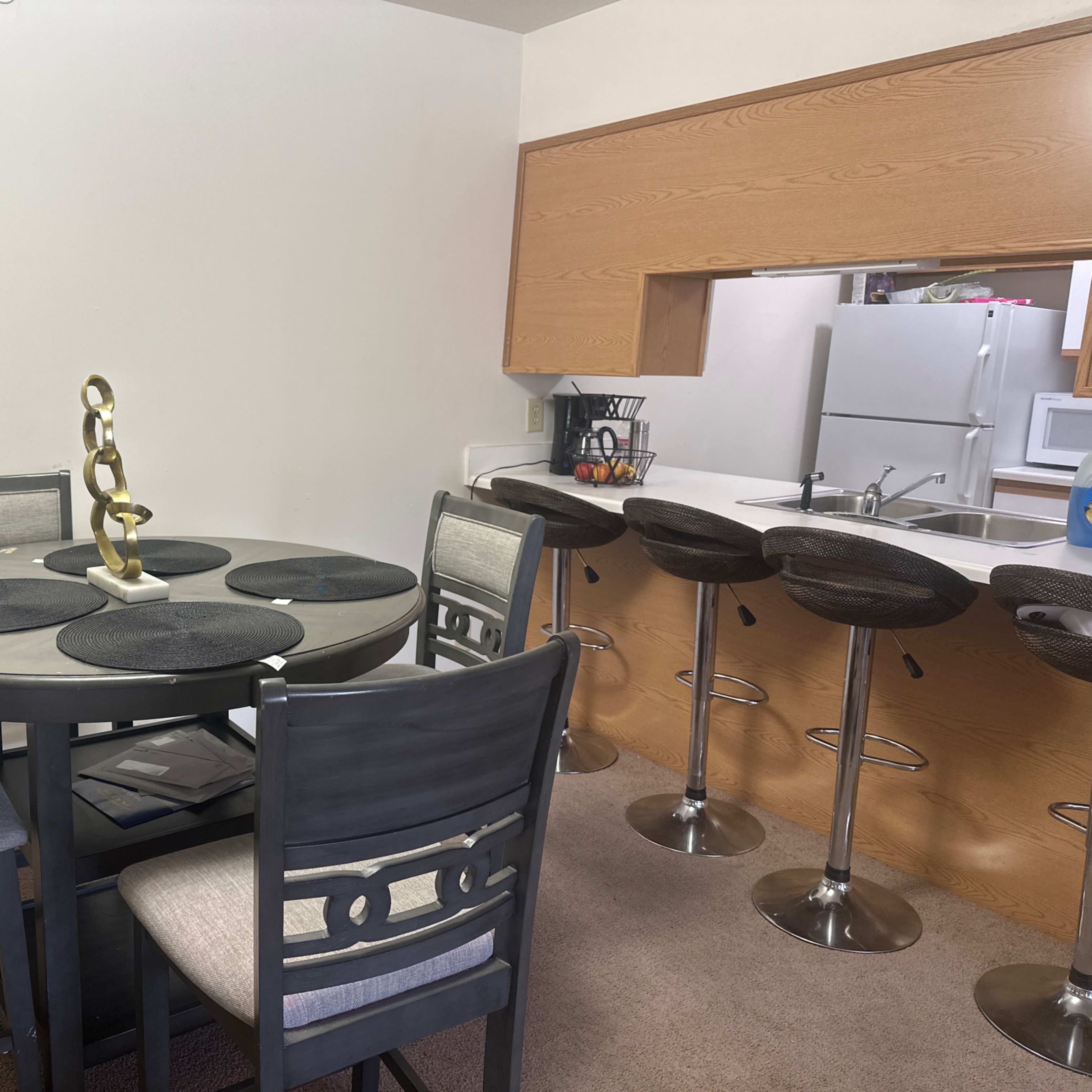 A dining area with a round table and four chairs, adjacent to a kitchen with bar stools and a counter.