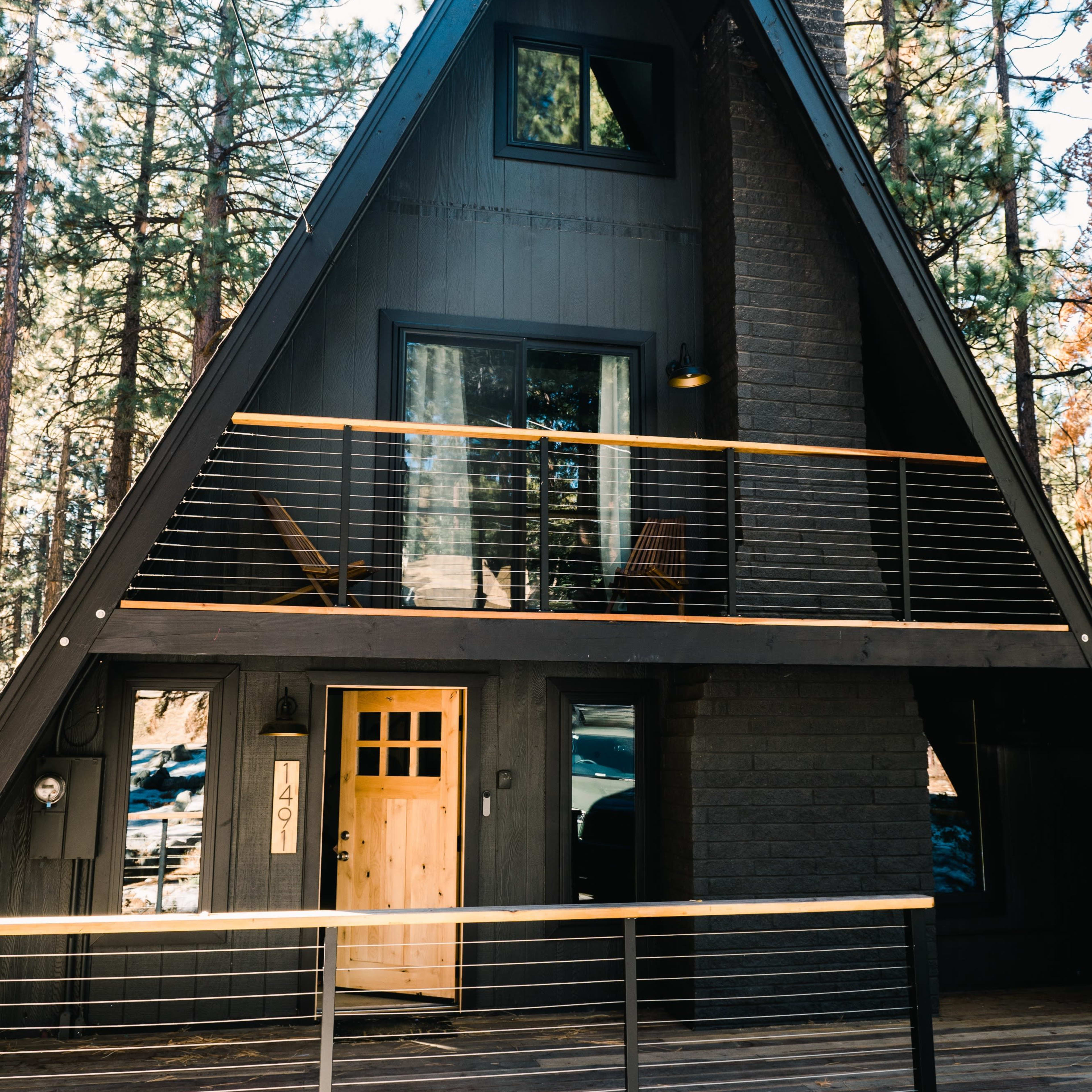 A modern A-frame house with large windows and a wooden entrance, situated among tall trees.