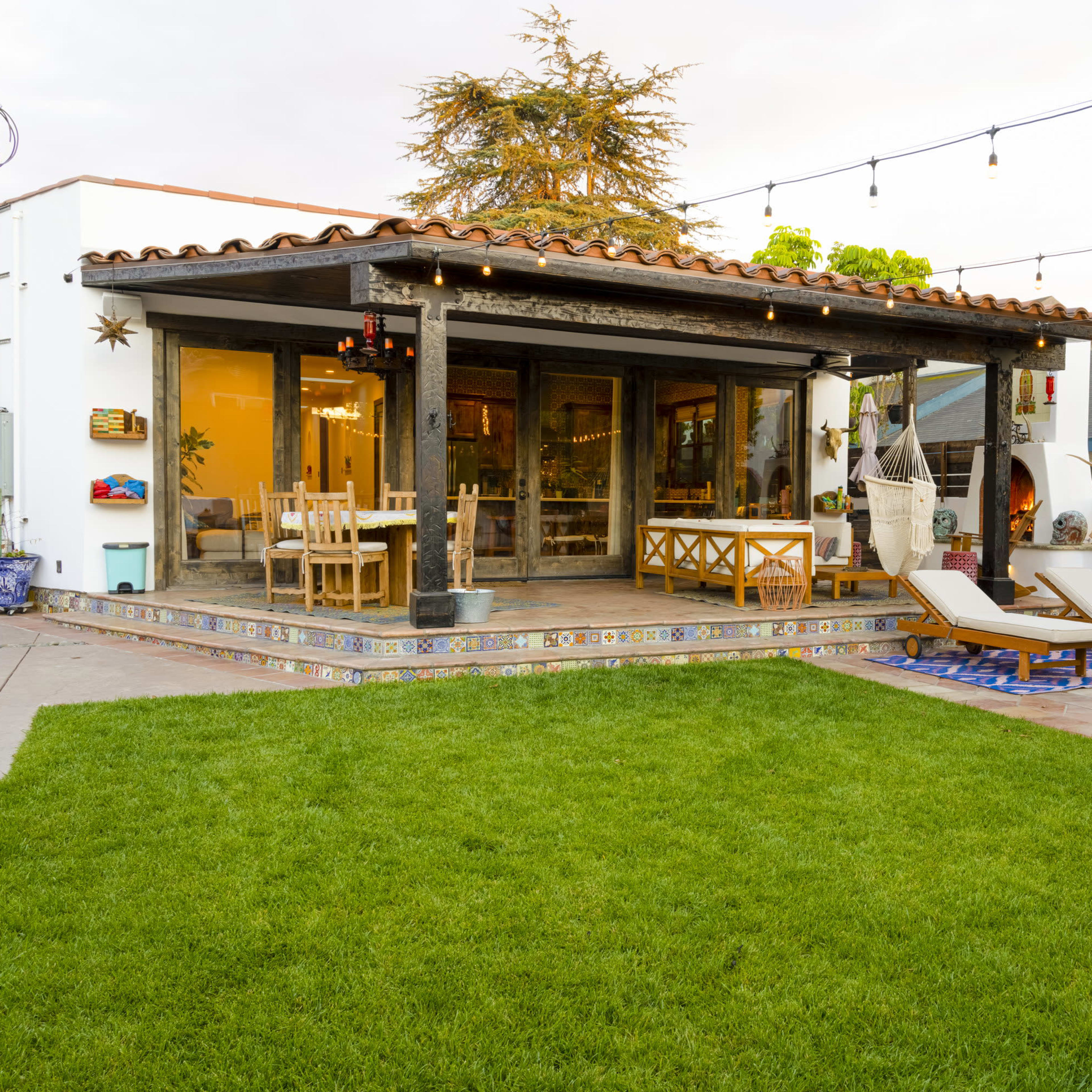 A single-story home with large windows and a covered patio overlooks a well-maintained lawn and a small pool, surrounded by colorful tiles.