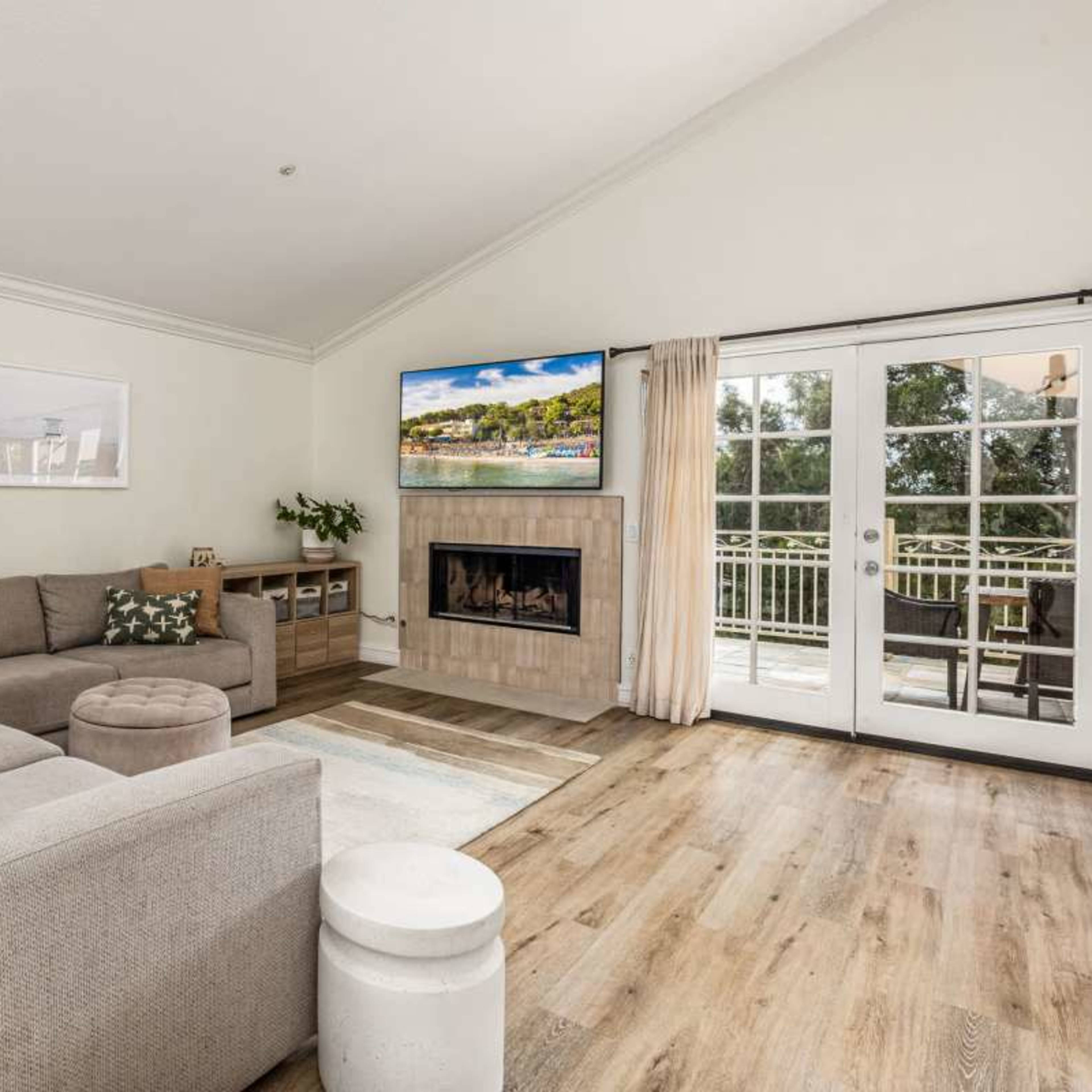 The living room features a sectional sofa, a fireplace, and large glass doors leading to a balcony.