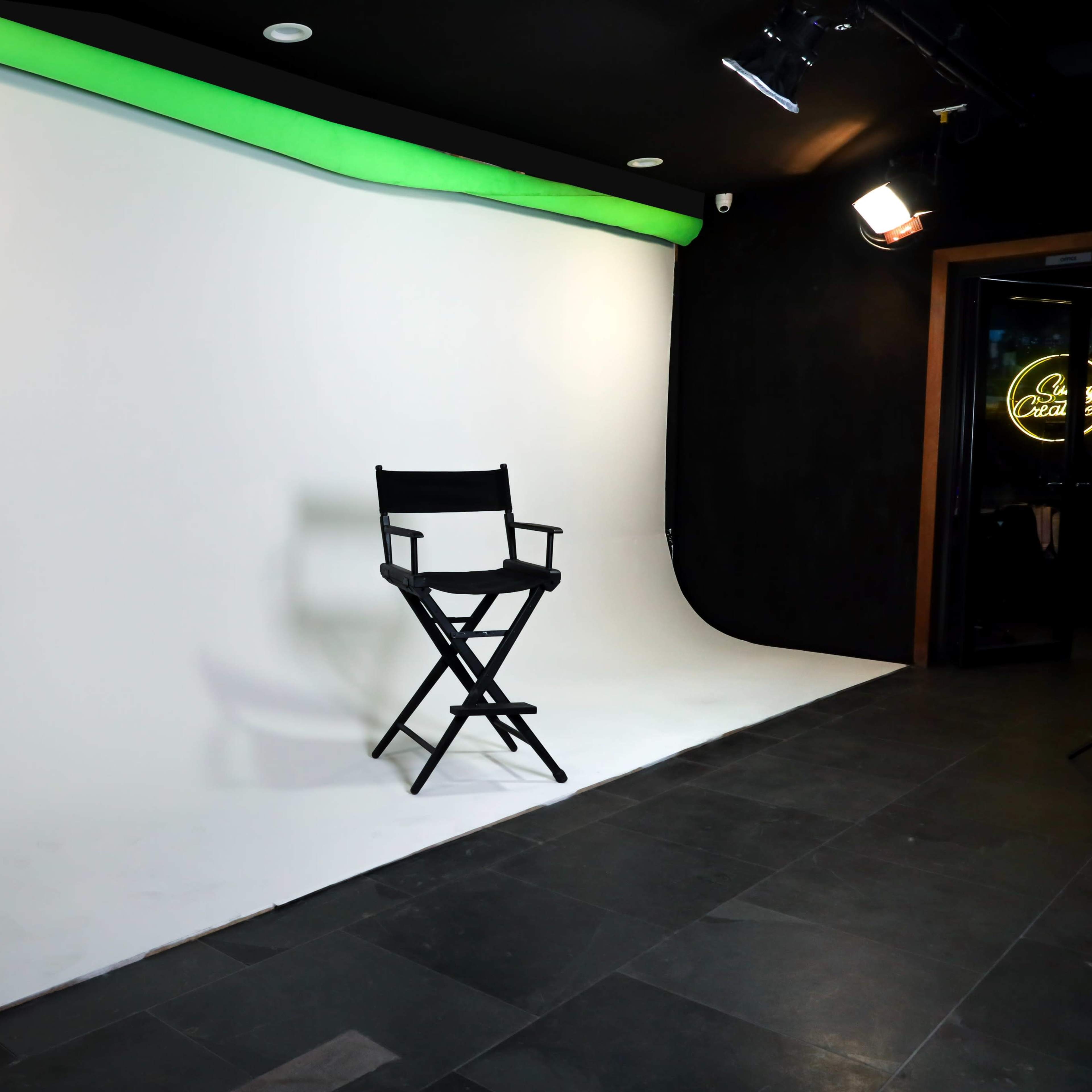 A black director's chair is positioned in front of a white backdrop with a green lighting strip at the top.