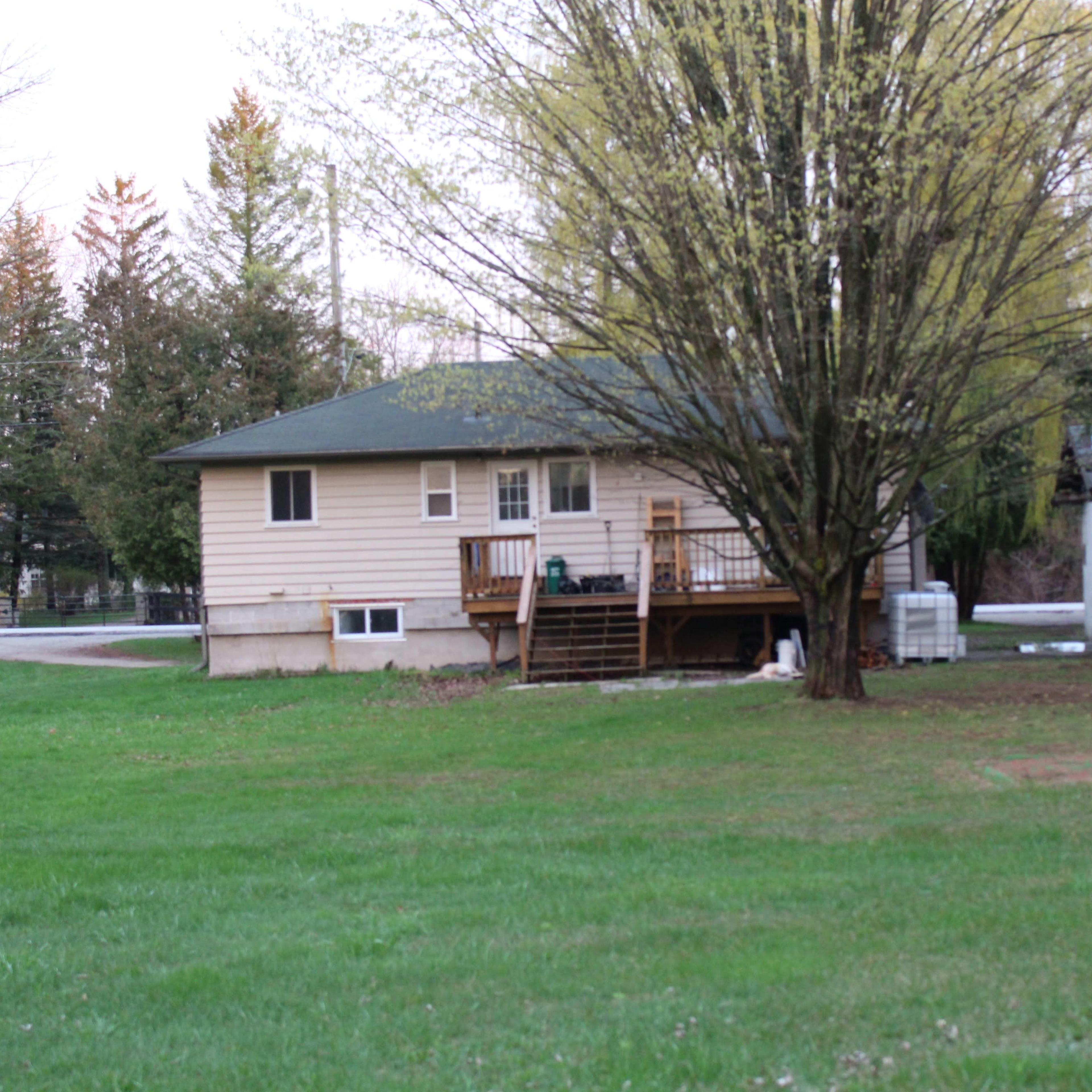 A single-story house with a front porch, surrounded by trees and a grassy yard.