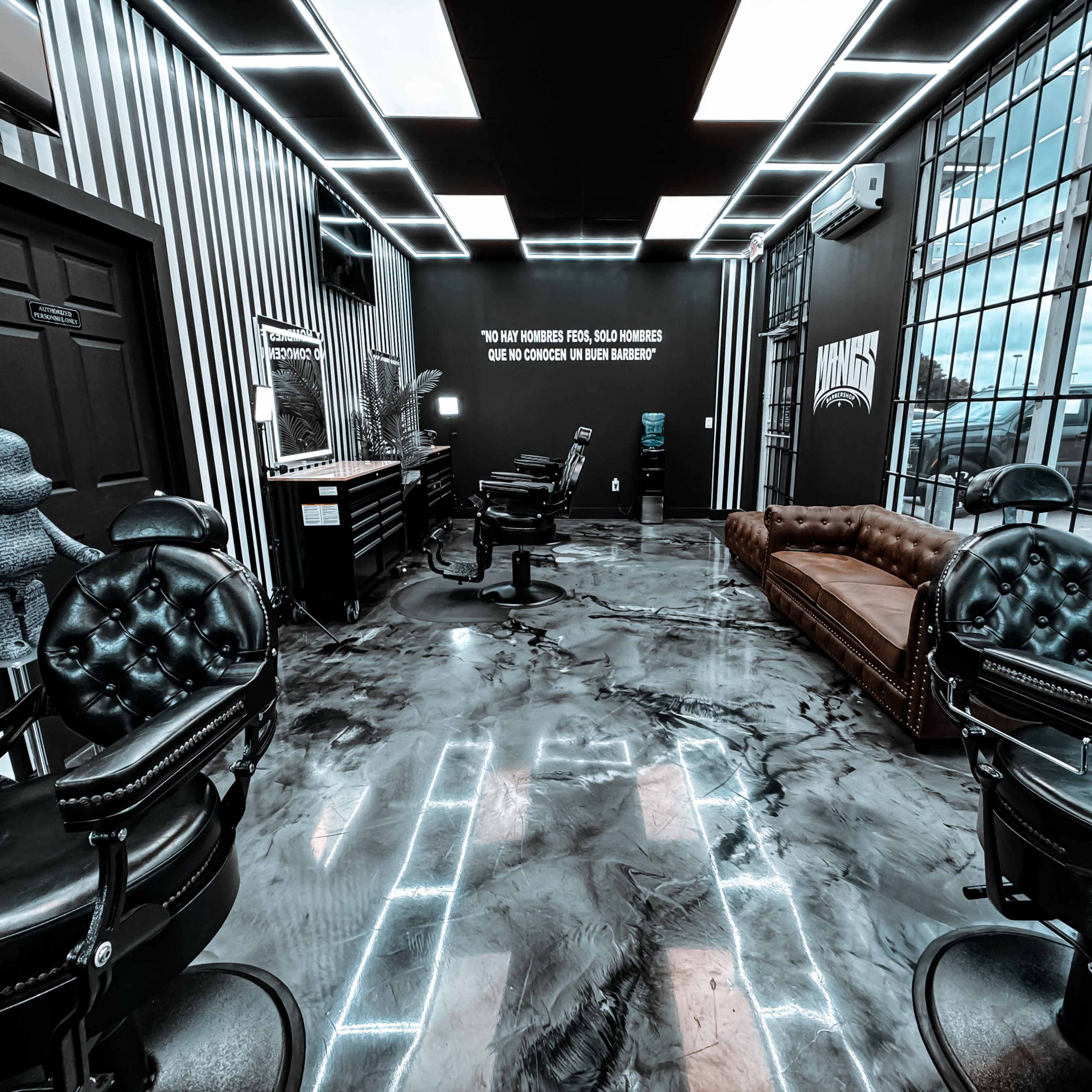 A modern barbershop interior with black and white striped walls, two barber chairs, a brown leather couch, and large windows with industrial grid design.