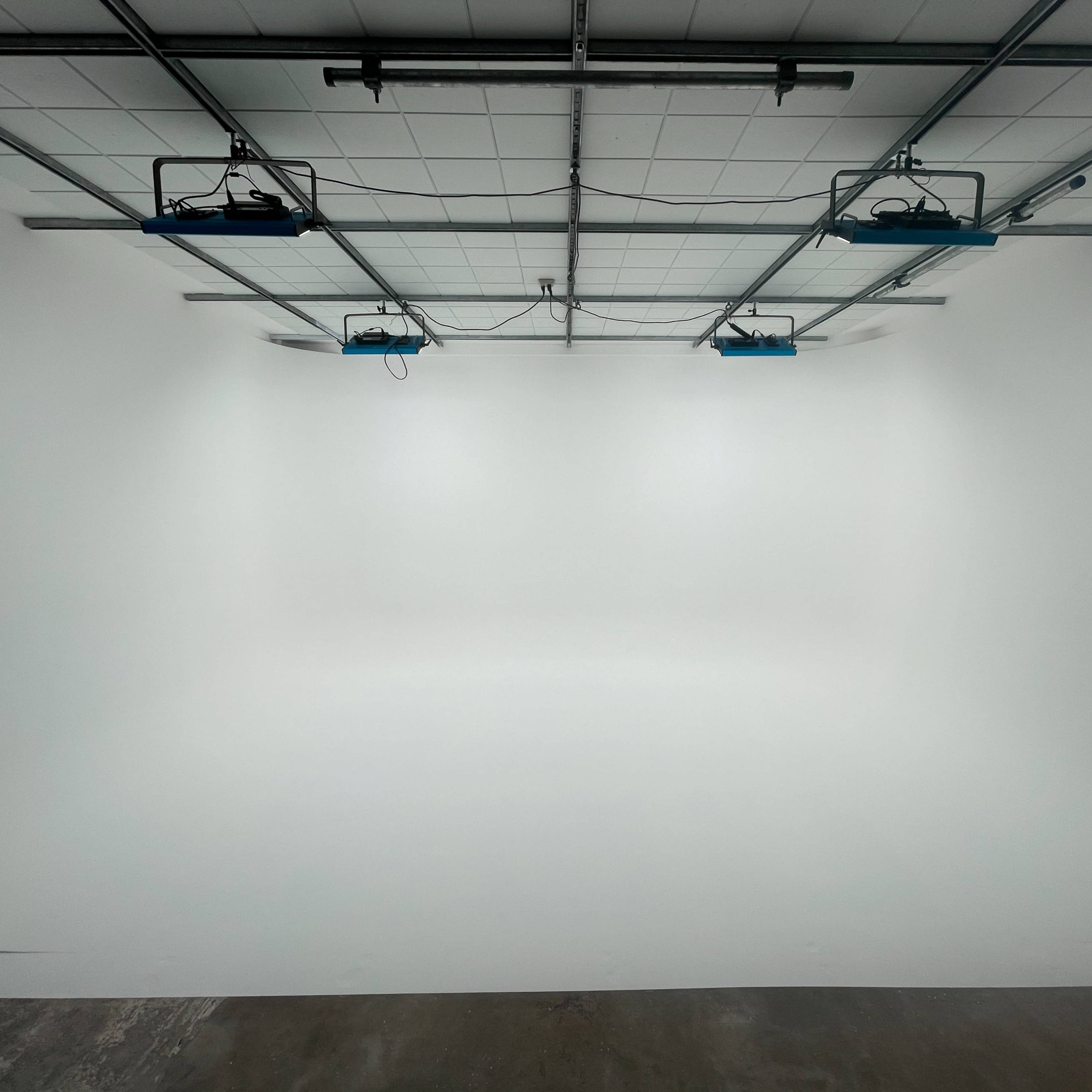 A spacious, empty studio with a smooth white backdrop and overhead lighting fixtures.