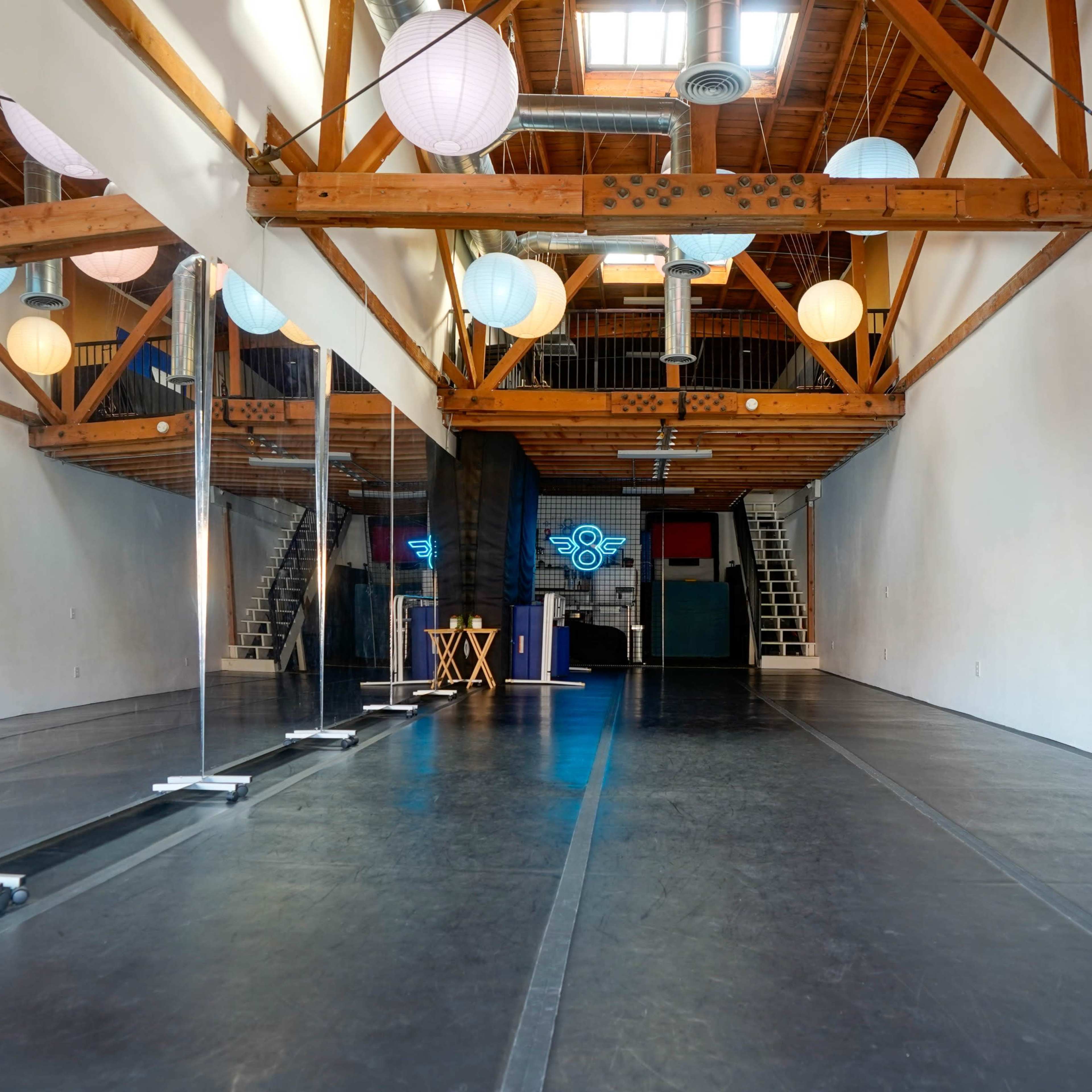 A spacious dance studio with wooden beams, large mirrors, and decorative paper lanterns hanging from the ceiling.
