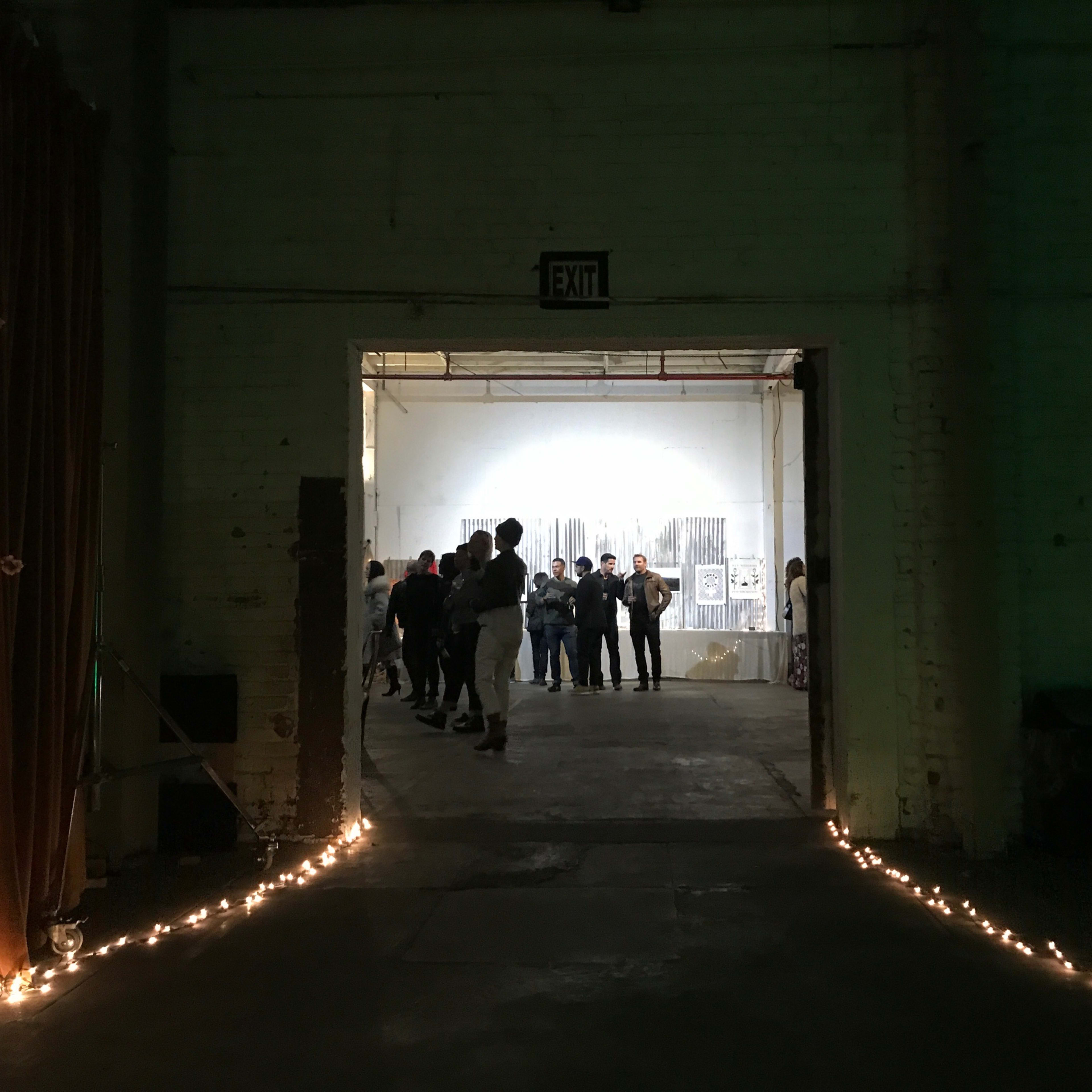 People are gathered in an industrial space, visible through an open doorway illuminated by string lights along the floor.