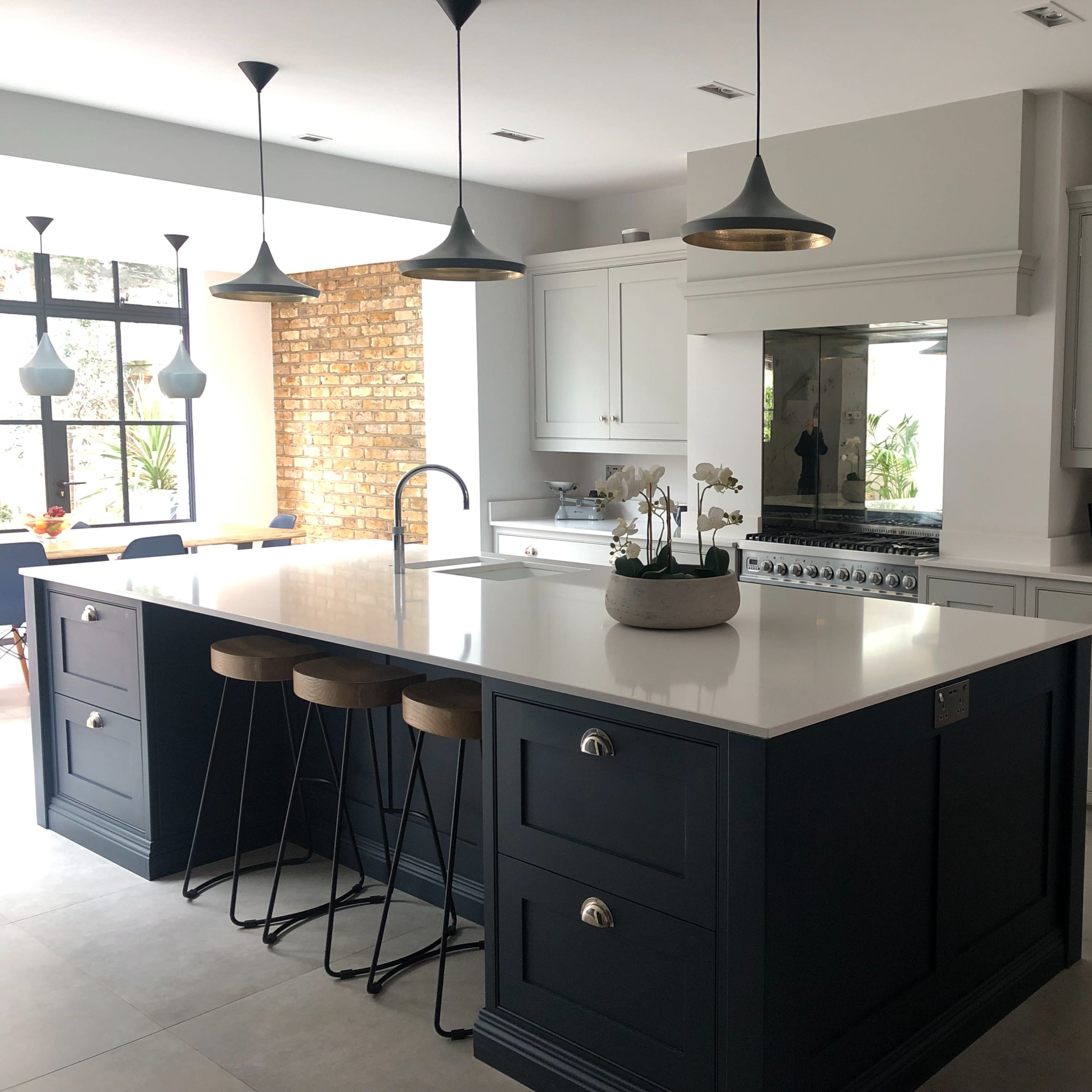 A modern kitchen featuring a central island with bar stools, light-colored cabinets, dark blue accents, and large windows letting in natural light.