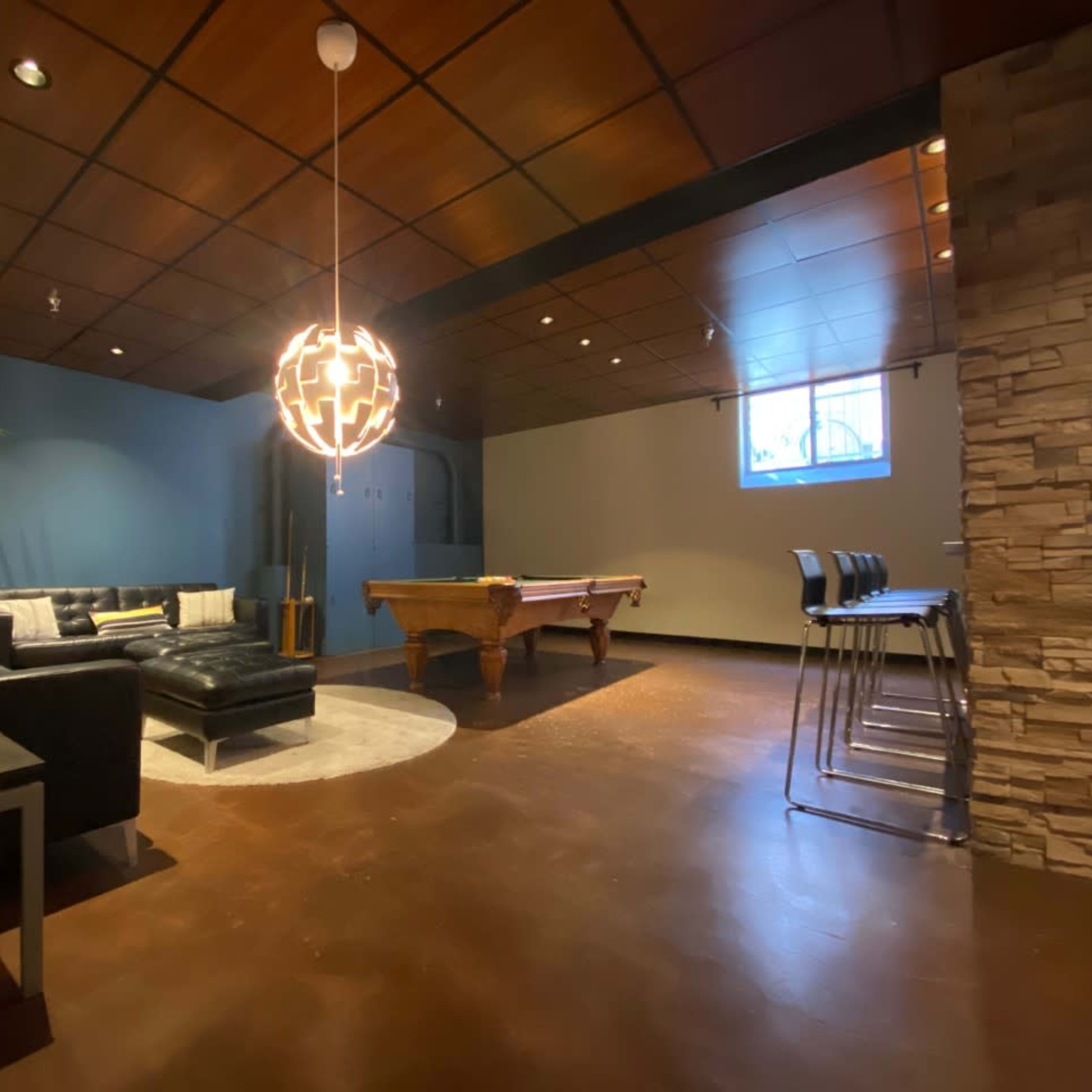 A game room features a pool table, a sectional sofa, and a modern light fixture hanging from the ceiling.