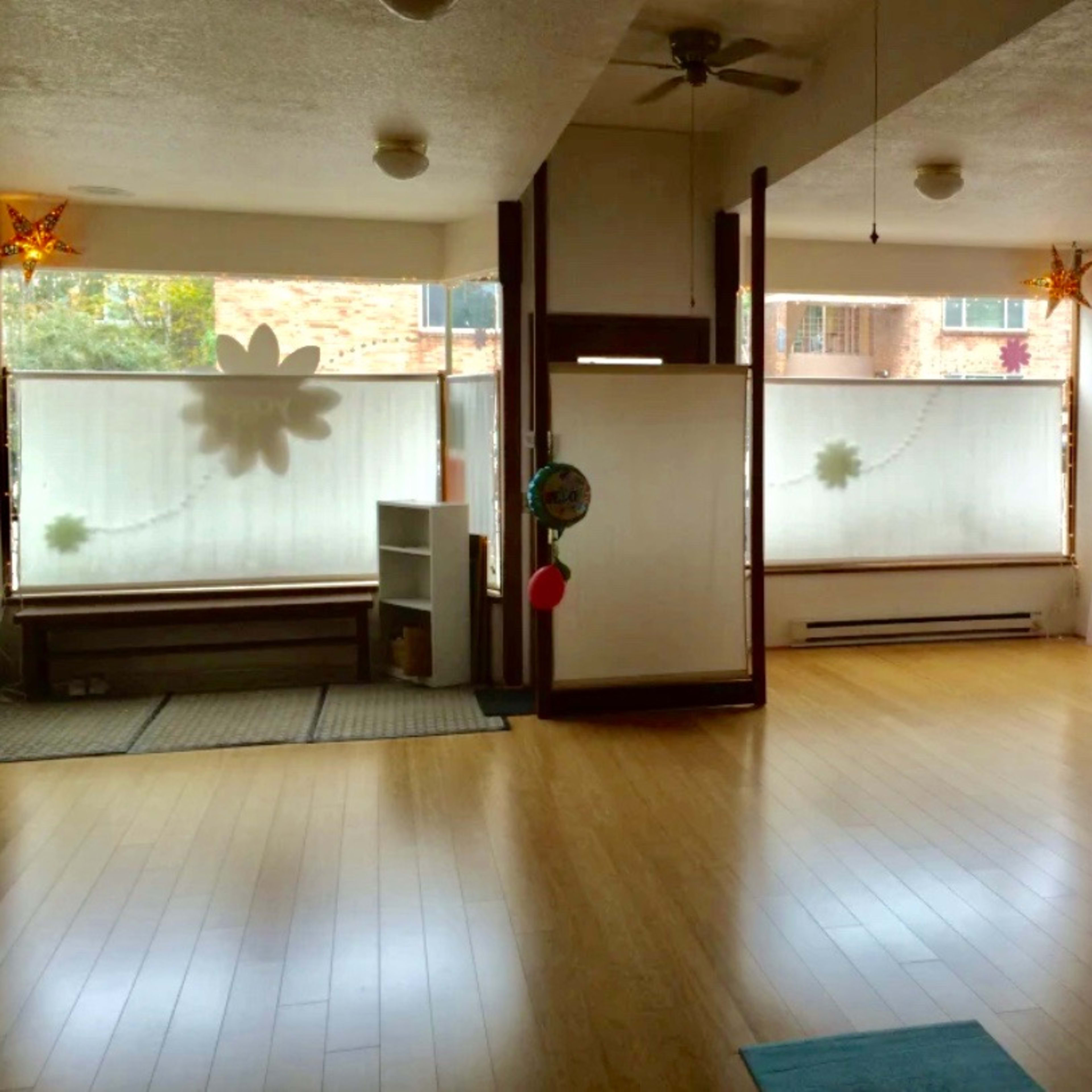 A spacious room with wooden flooring, large windows covered by sheer curtains, and a simple partition separating different areas.