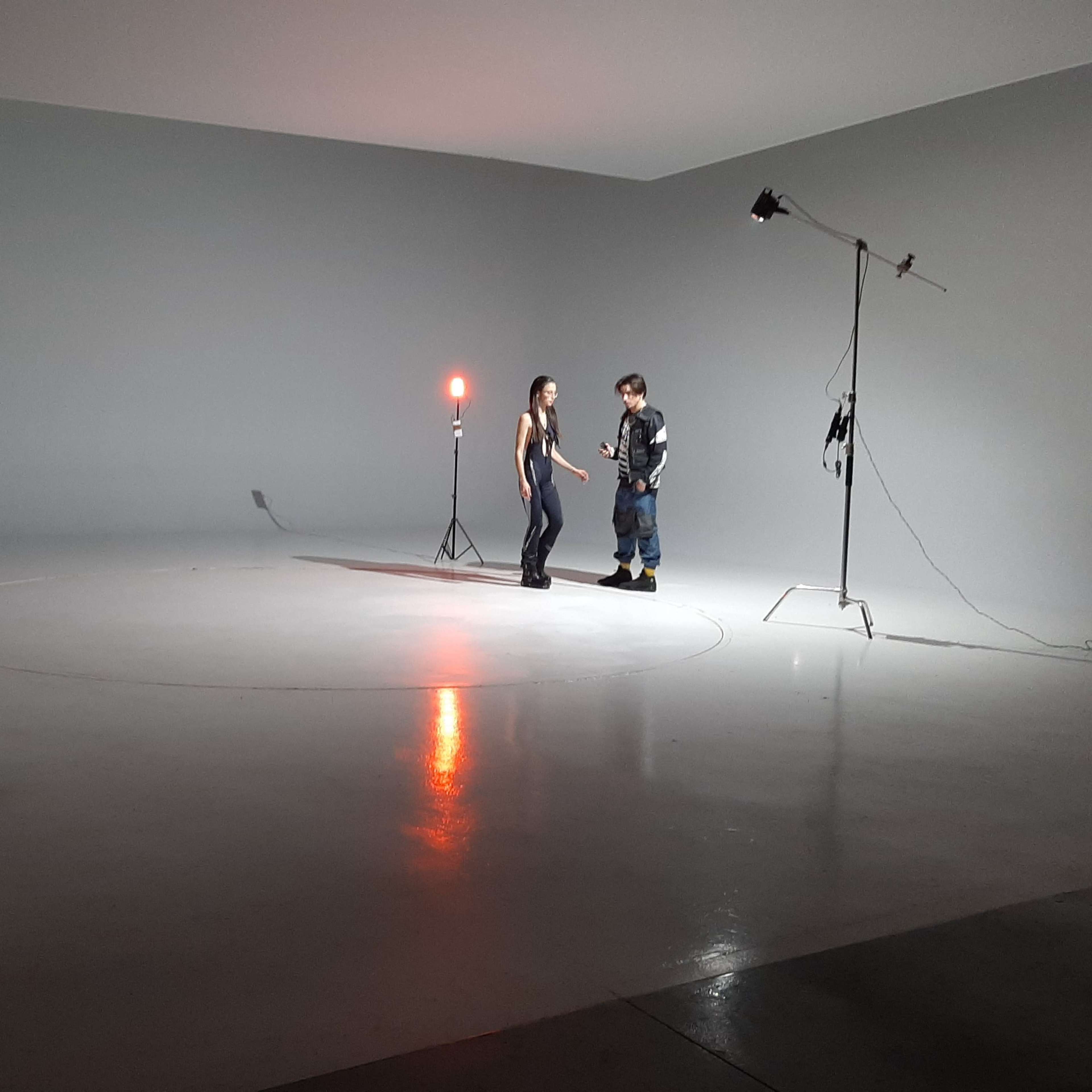 A photographer captures two people engaged in a conversation in a minimally lit studio space.