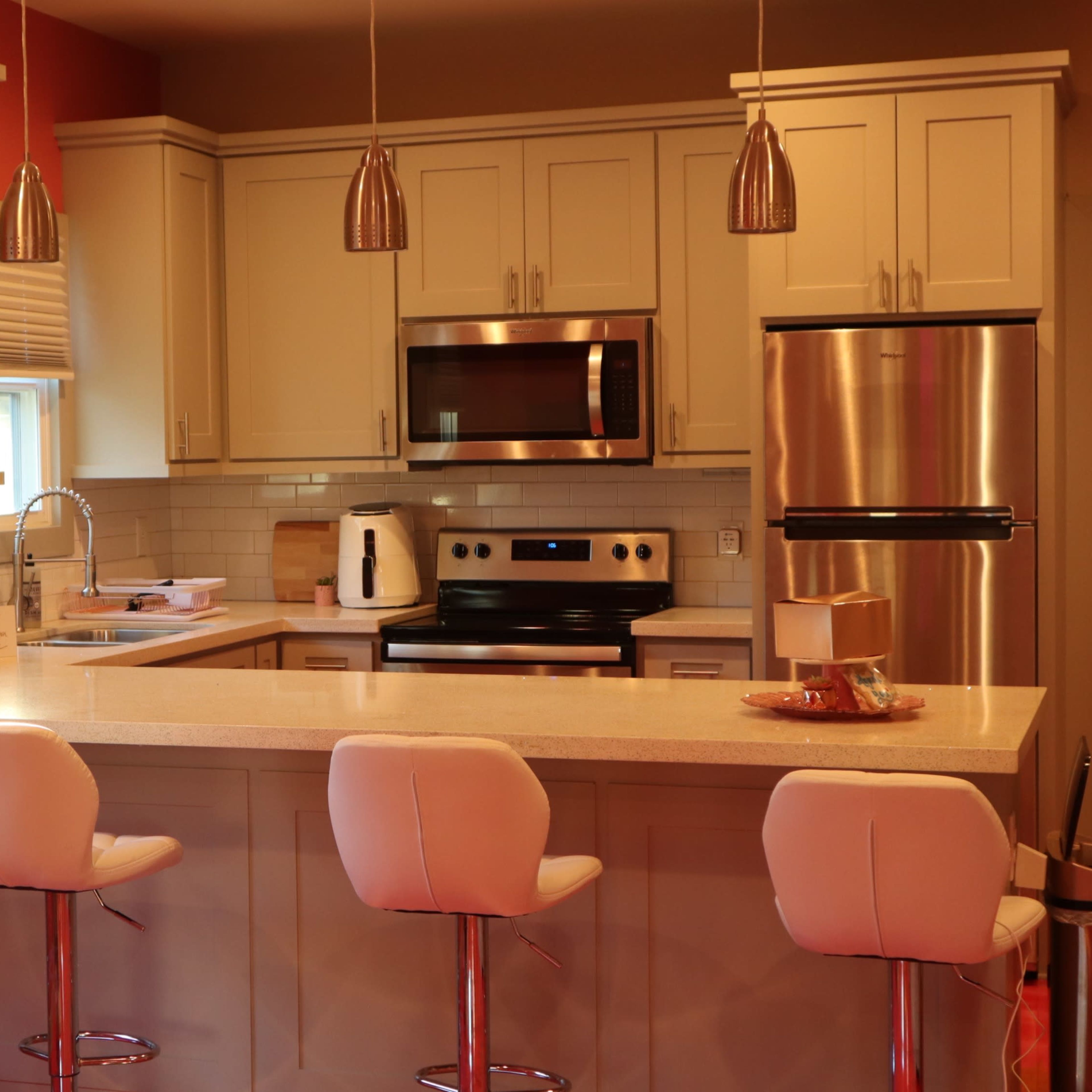 A modern kitchen with light-colored cabinets, stainless steel appliances, and a central island with four white bar stools.