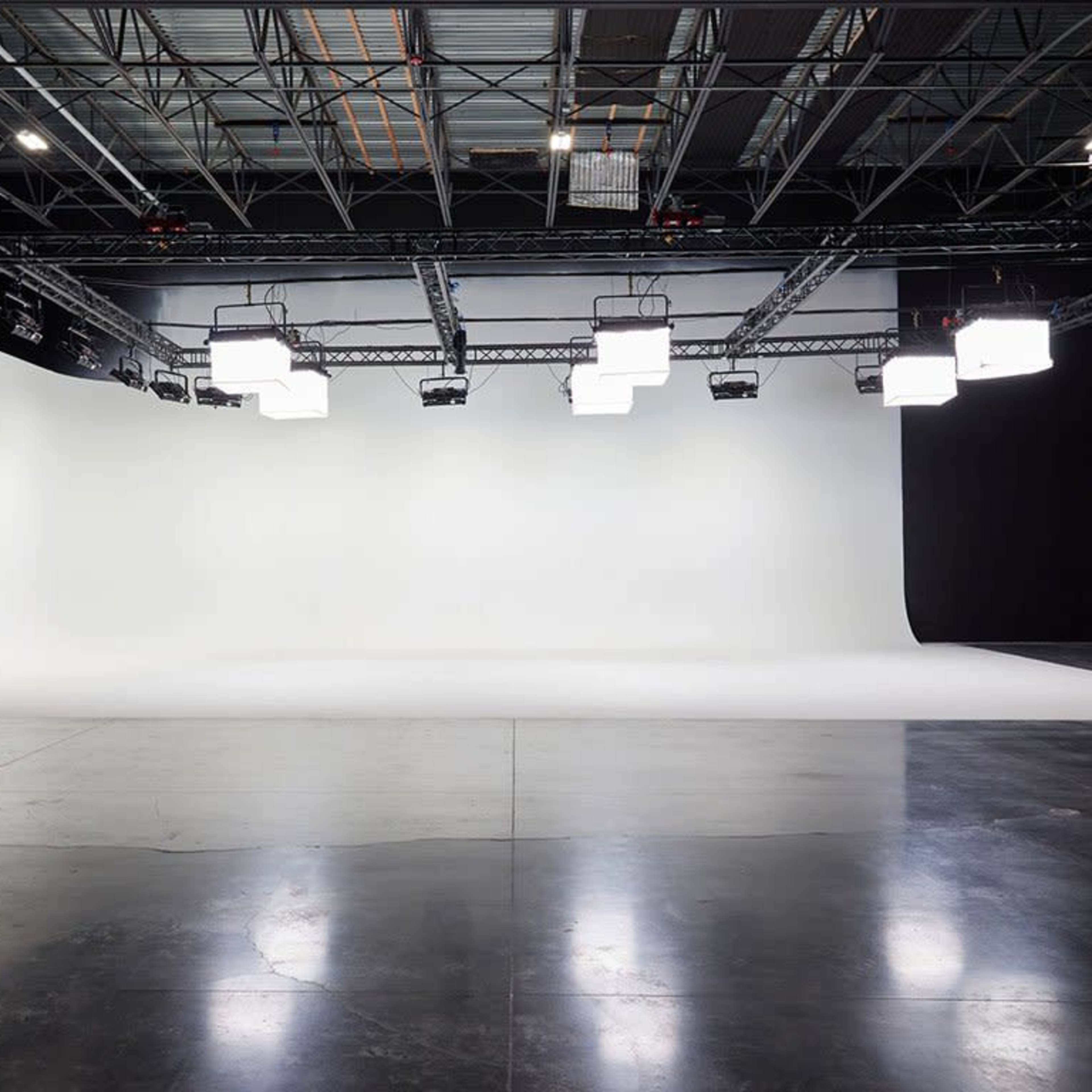 A spacious photography studio with a curved white backdrop and overhead lights.