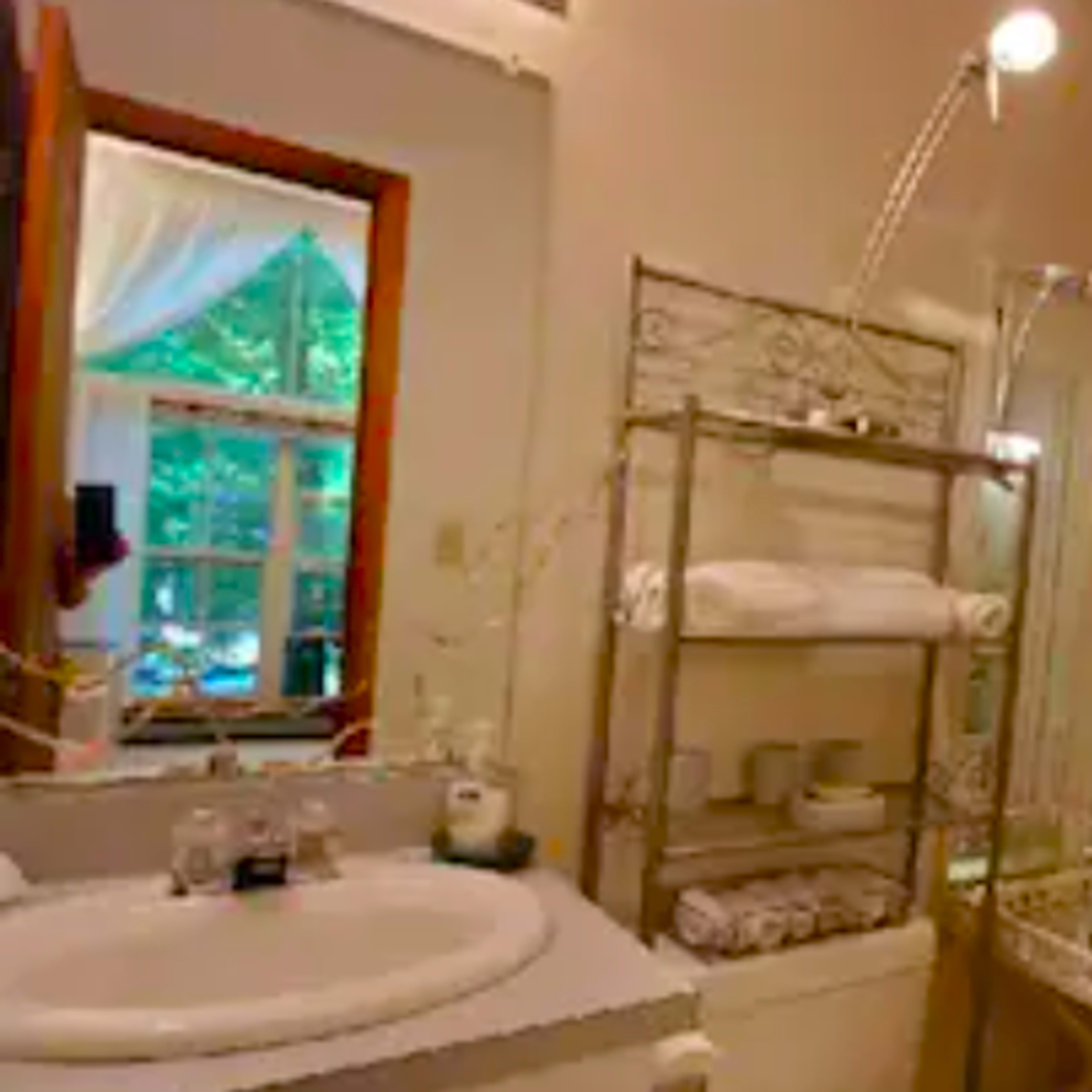 A well-lit bathroom featuring a bathtub, a shower stall, a shelving unit with towels, and a large mirror.