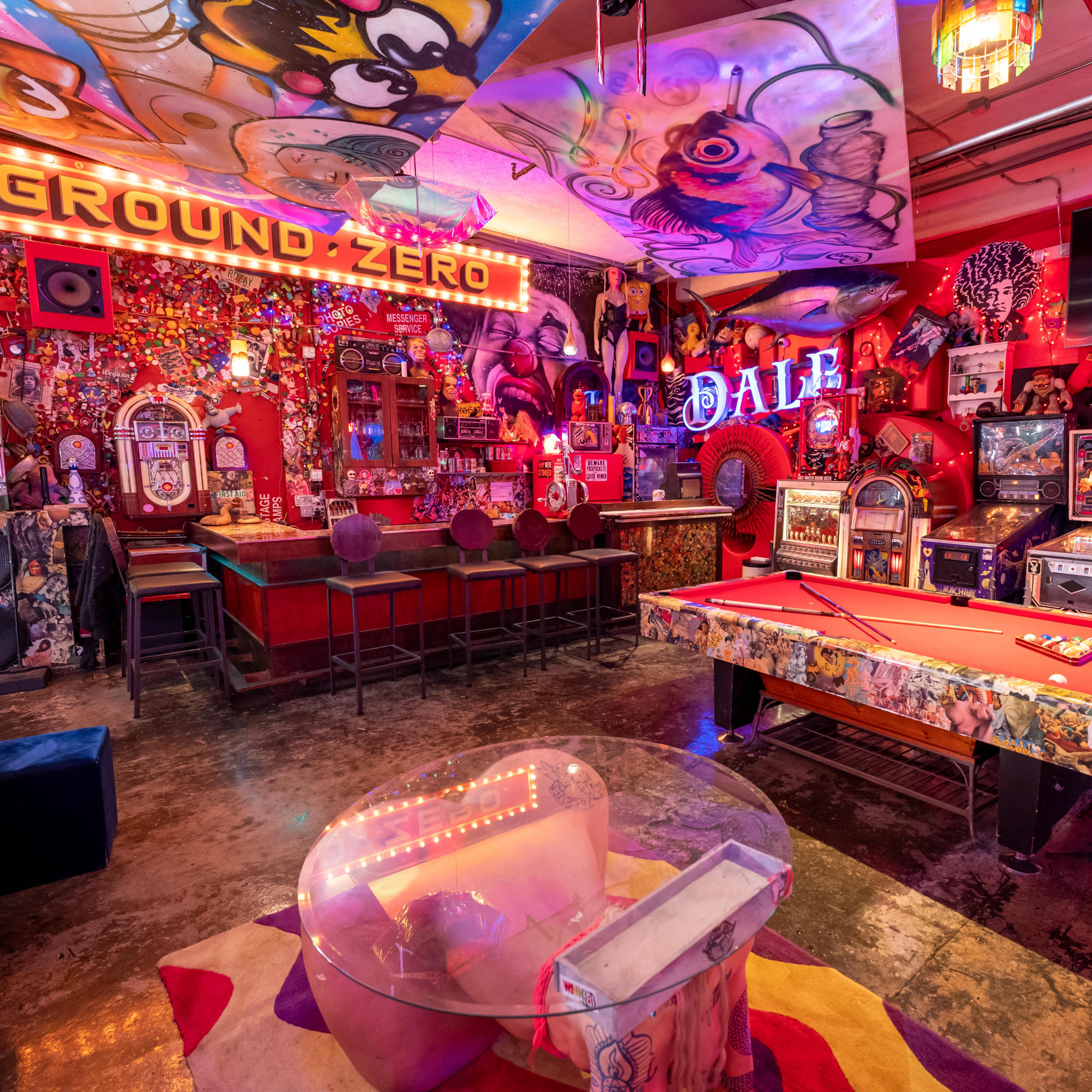 The scene depicts a vibrant game room filled with colorful decorations, an illuminated bar area, arcade machines, and a billiards table.