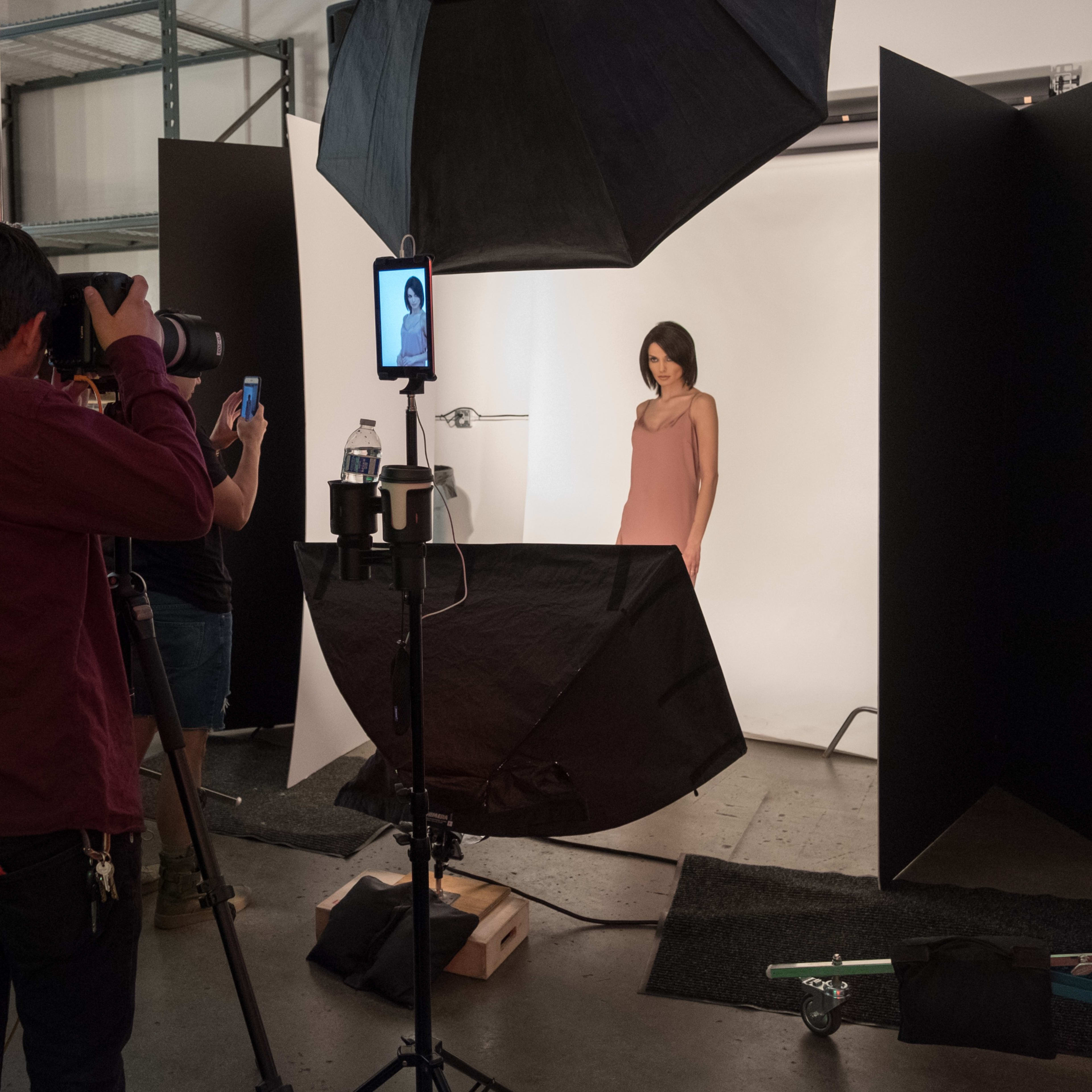 A photographer captures a model in a studio setting, with lighting equipment and backdrops arranged to create a professional photo shoot.