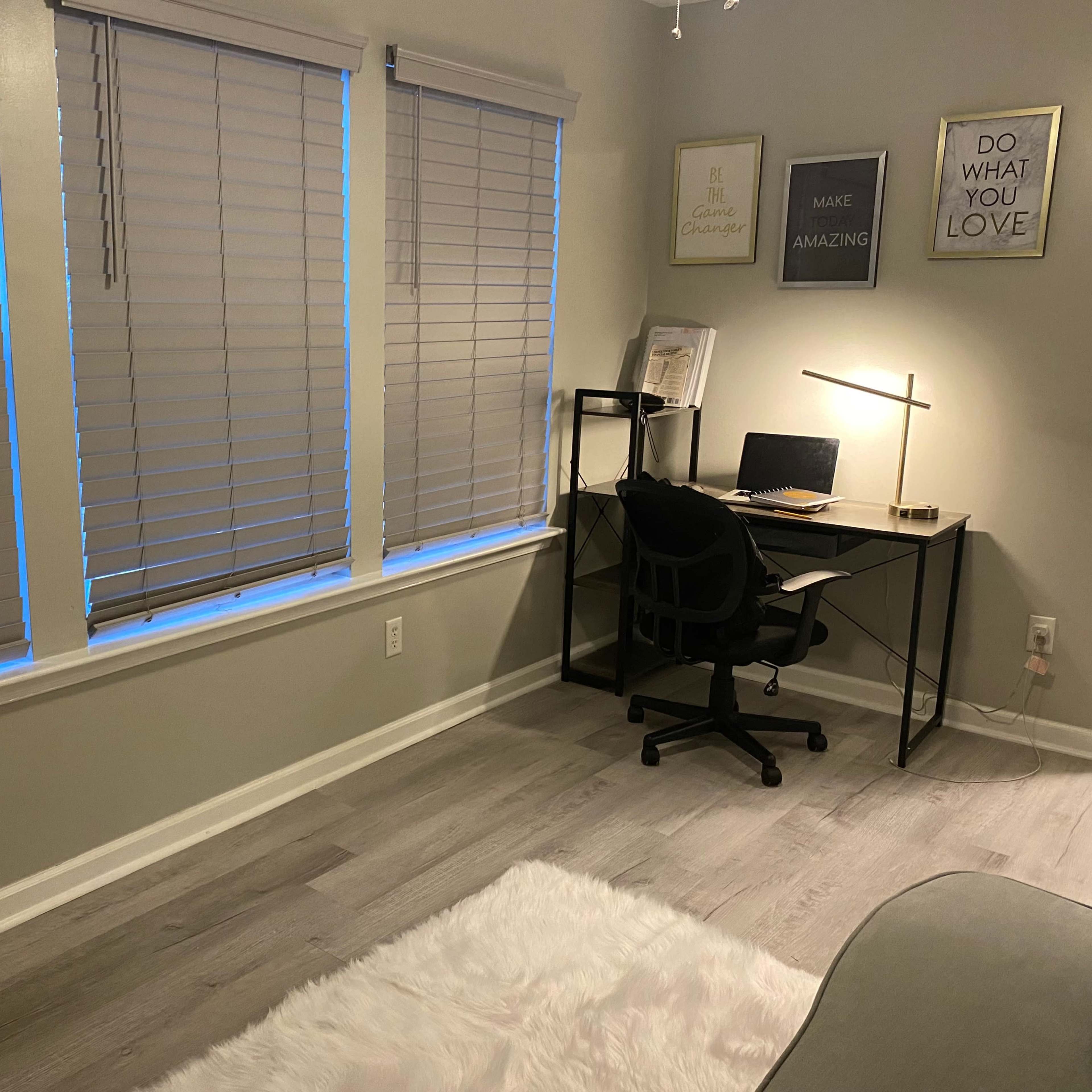 A modern home office with a desk, a chair, and window blinds, illuminated by soft blue light from outside.