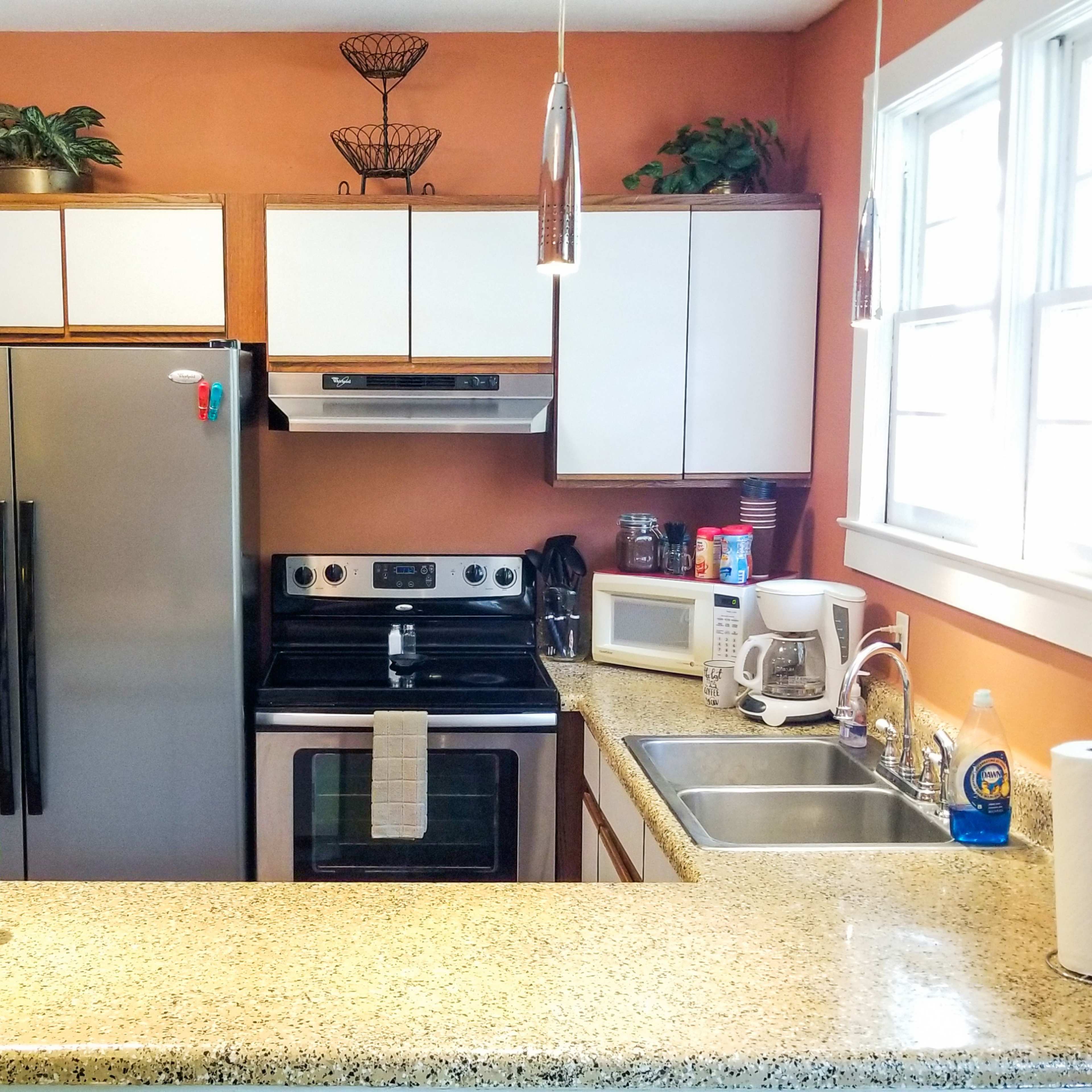 A modern kitchen features a granite countertop, stainless steel appliances, and orange walls with white cabinets.