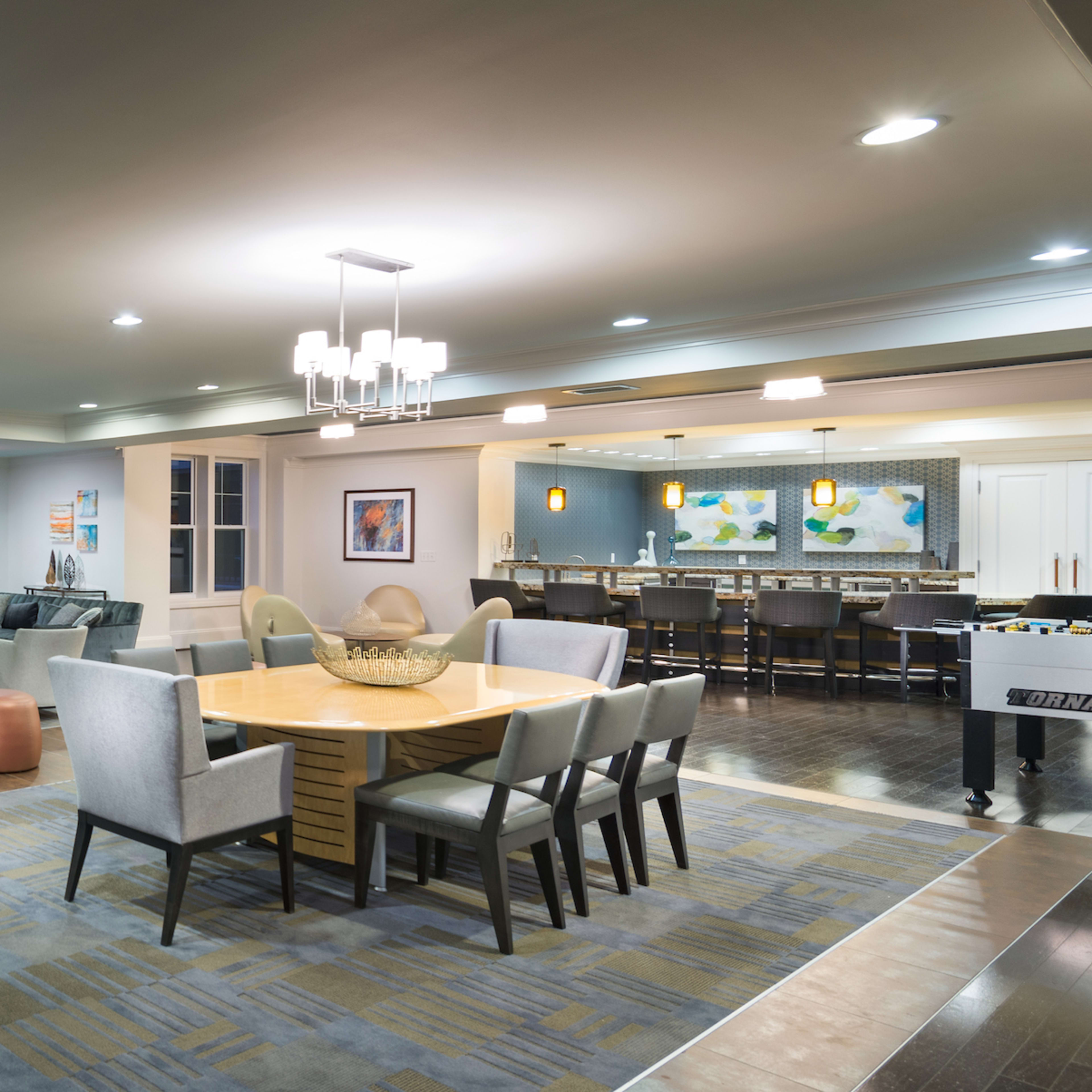 A spacious common area featuring a dining table, comfortable seating, a fireplace, and a pool table, with modern decor and ambient lighting.