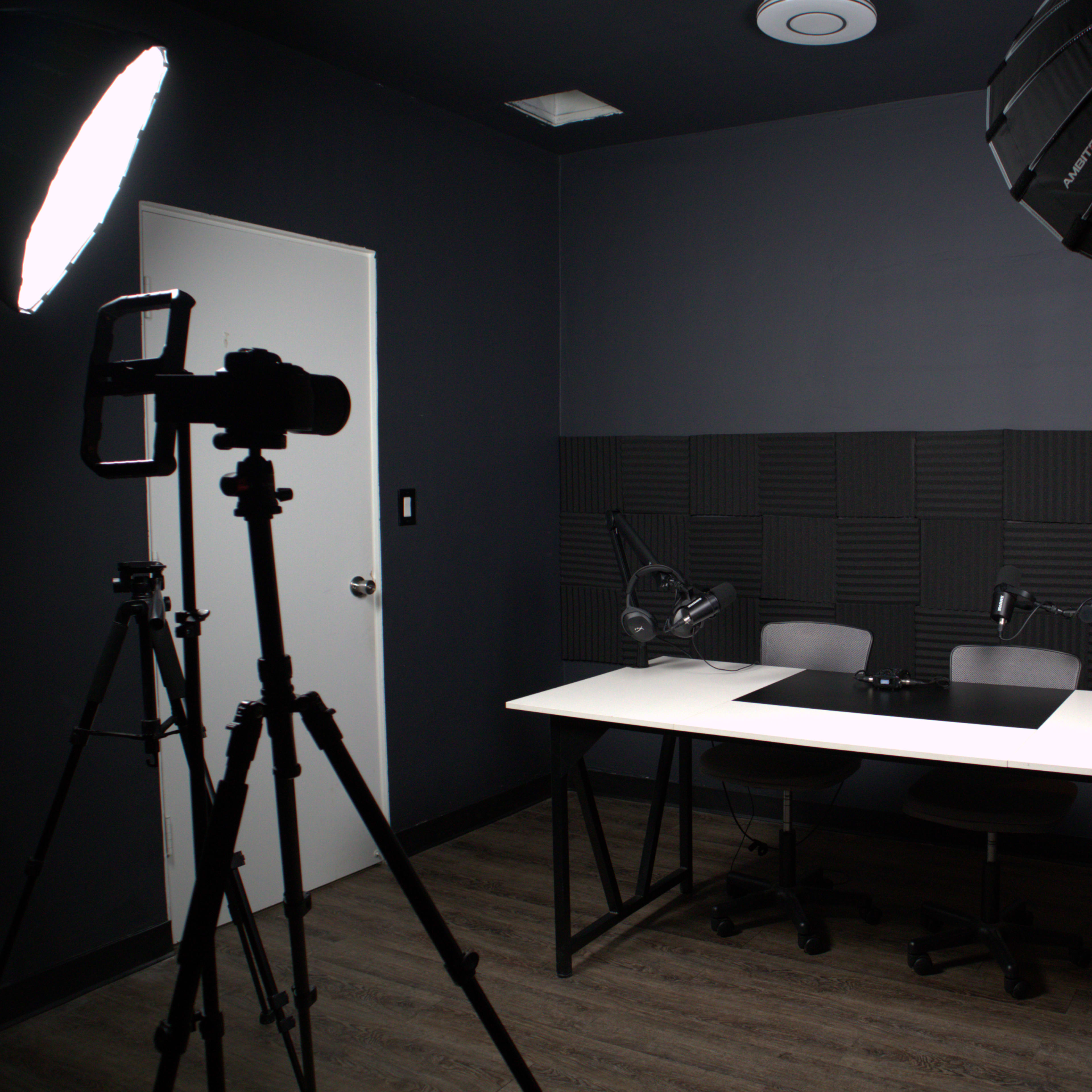 A dimly lit recording studio with two chairs and a table, equipped with lighting and audio equipment.