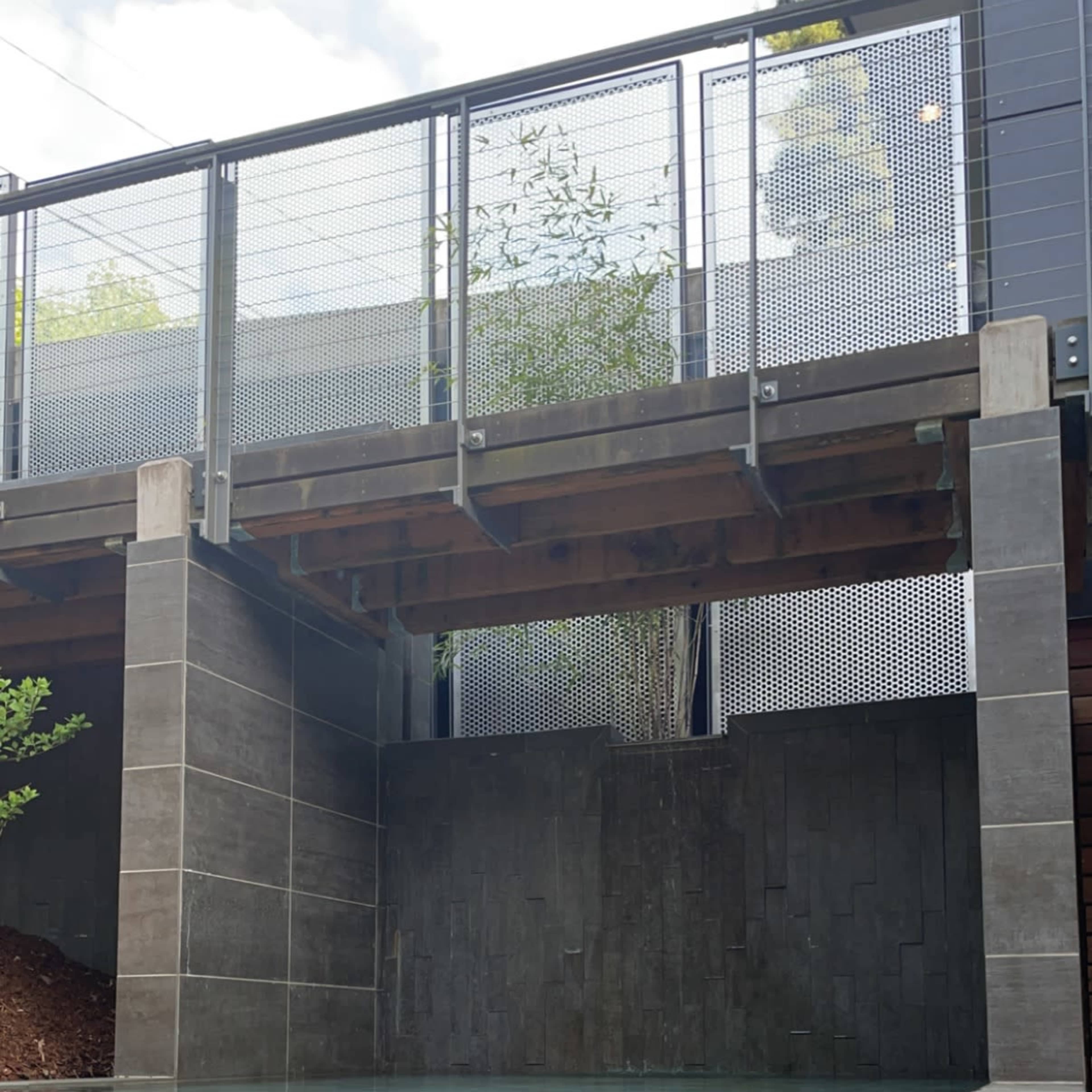 A modern pool area with a concrete structure overhead, surrounded by stone walls and a wooden deck.