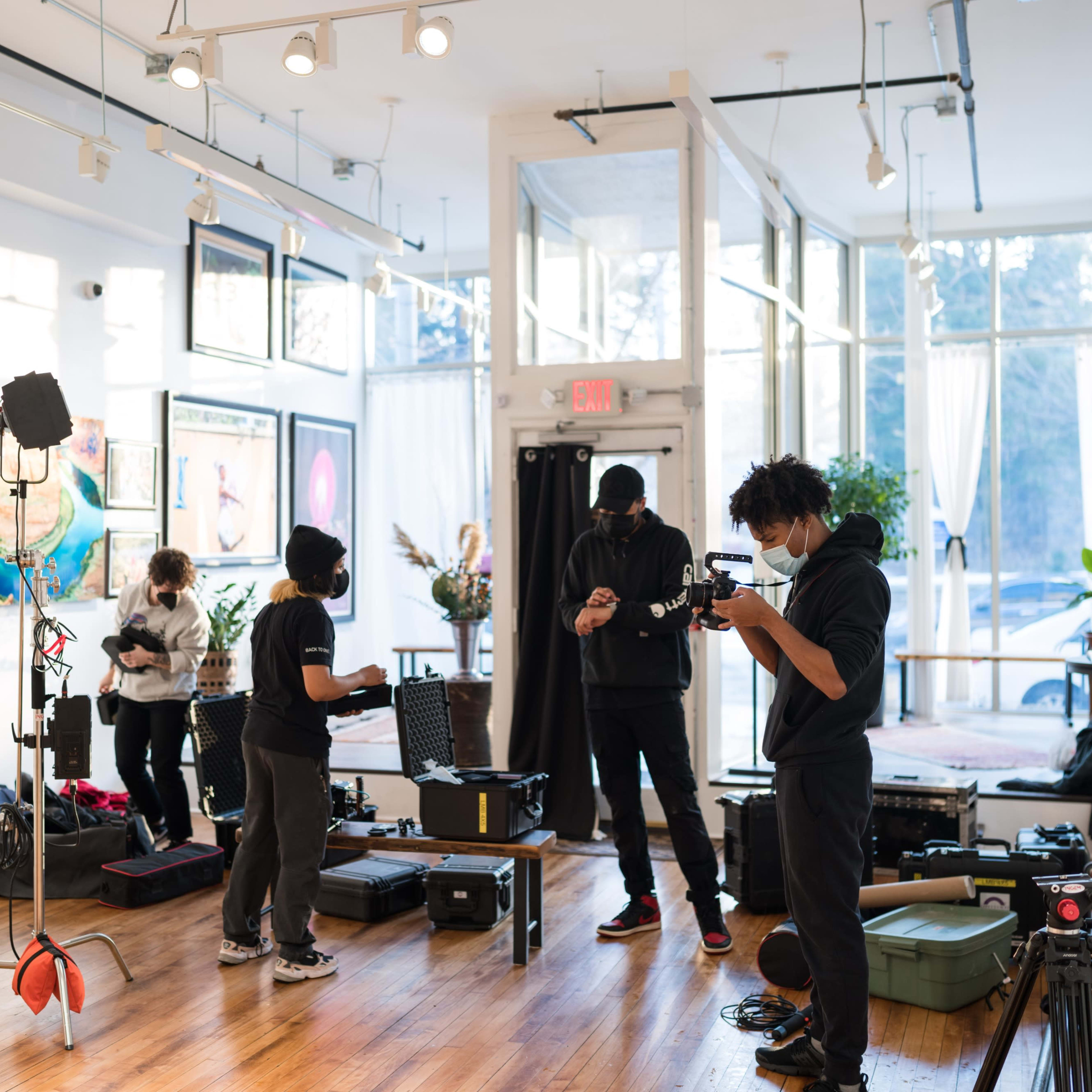 A film crew sets up equipment inside a bright studio, preparing for a shoot amidst various lighting and camera gear.
