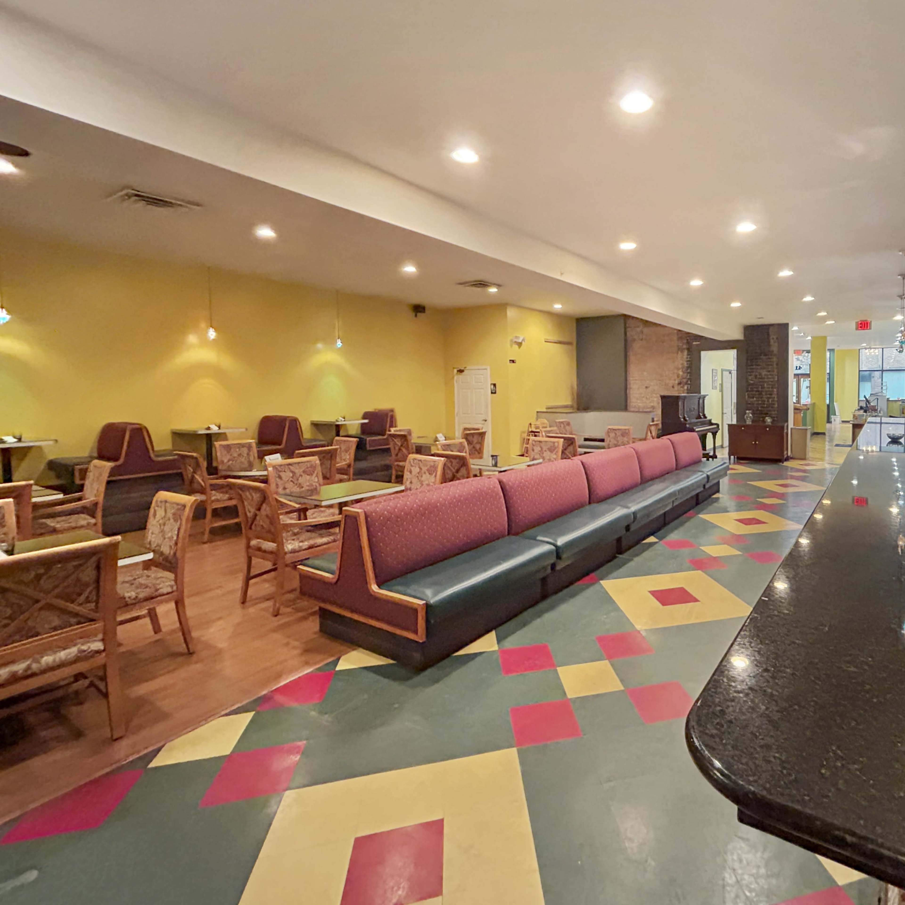 A spacious café with colorful tiled flooring, a long bar counter, and seating areas featuring a mix of chairs and tables.