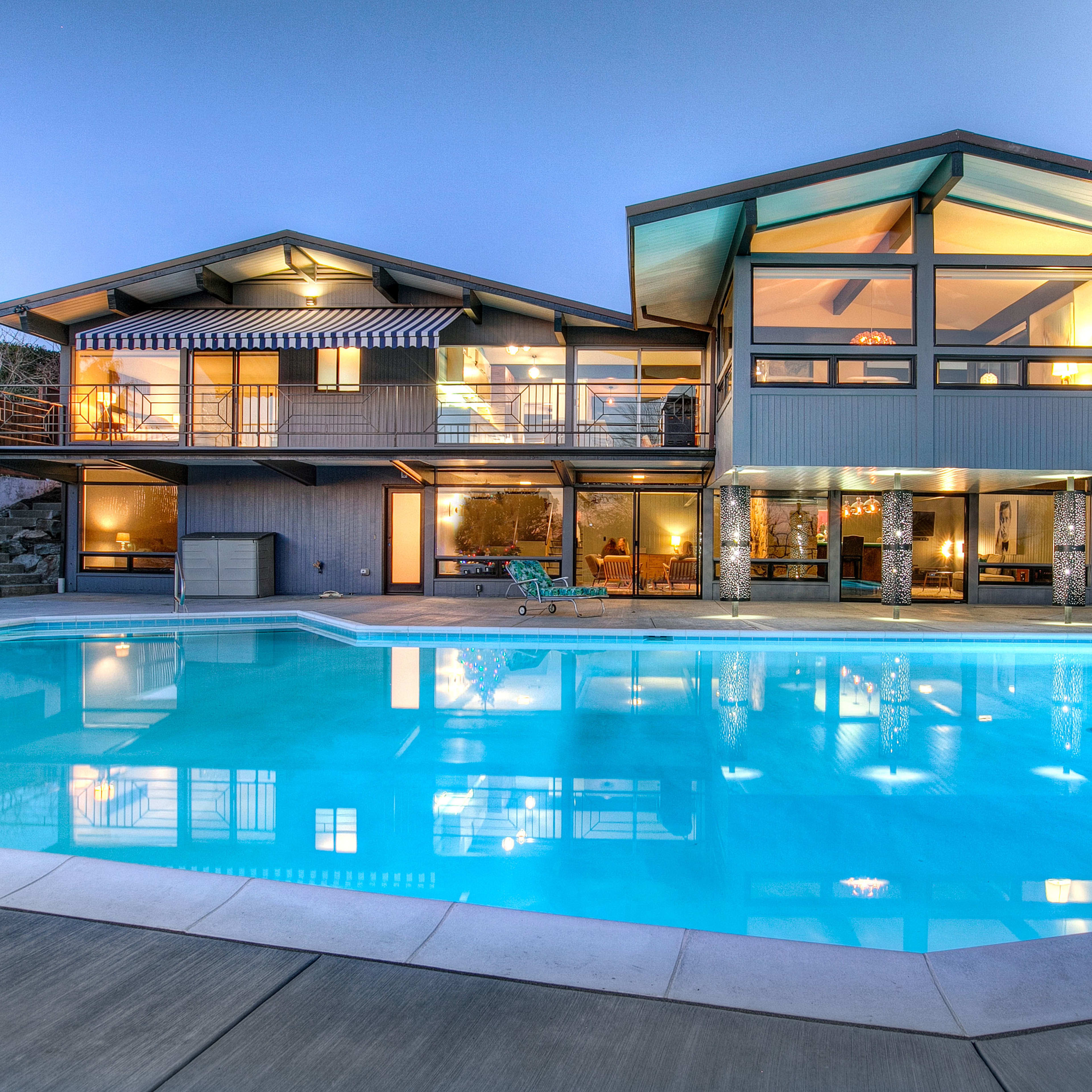 A modern two-story house with large windows, overlooking a rectangular swimming pool.