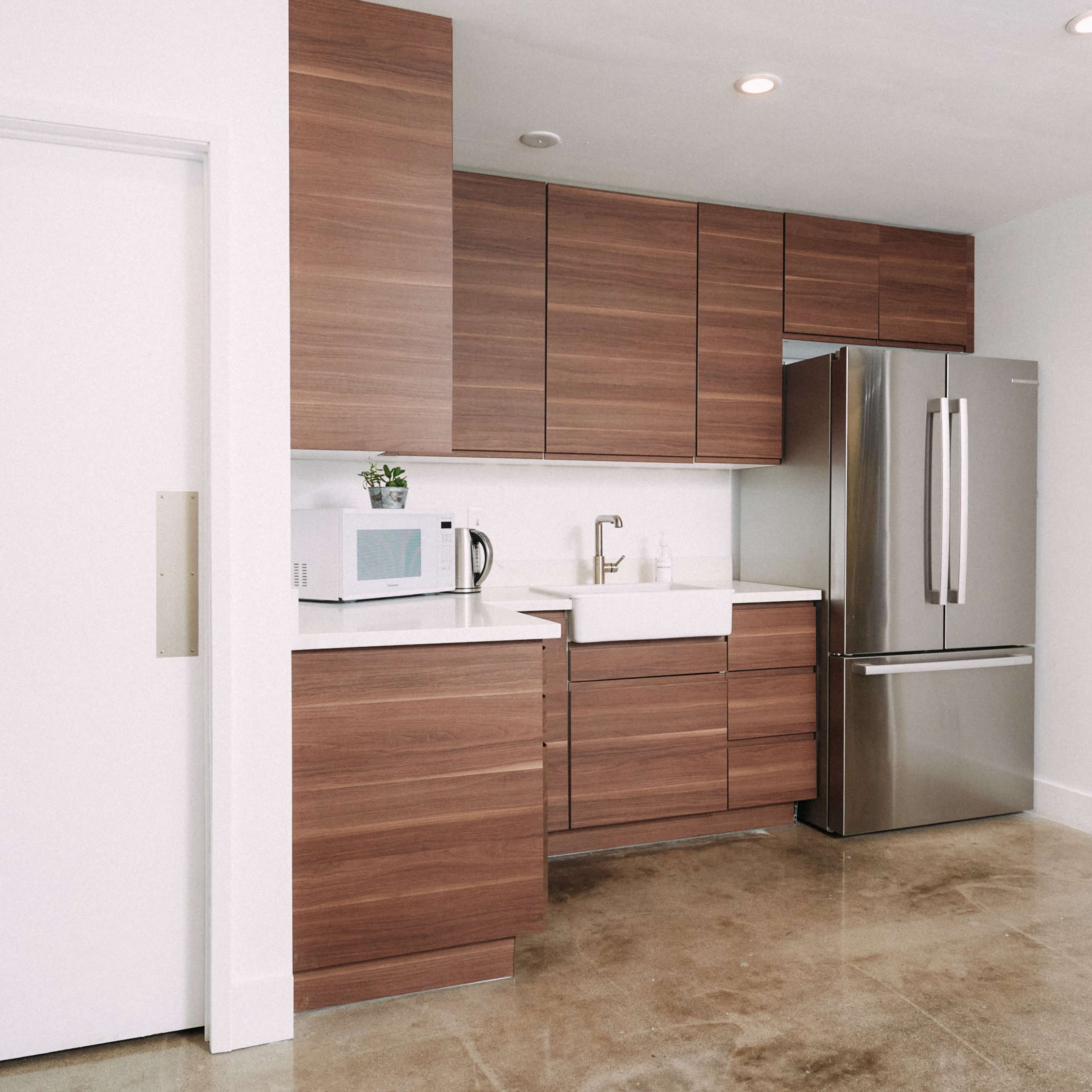 A modern kitchen featuring wooden cabinets, a stainless steel refrigerator, a white sink, and a microwave on the countertop.