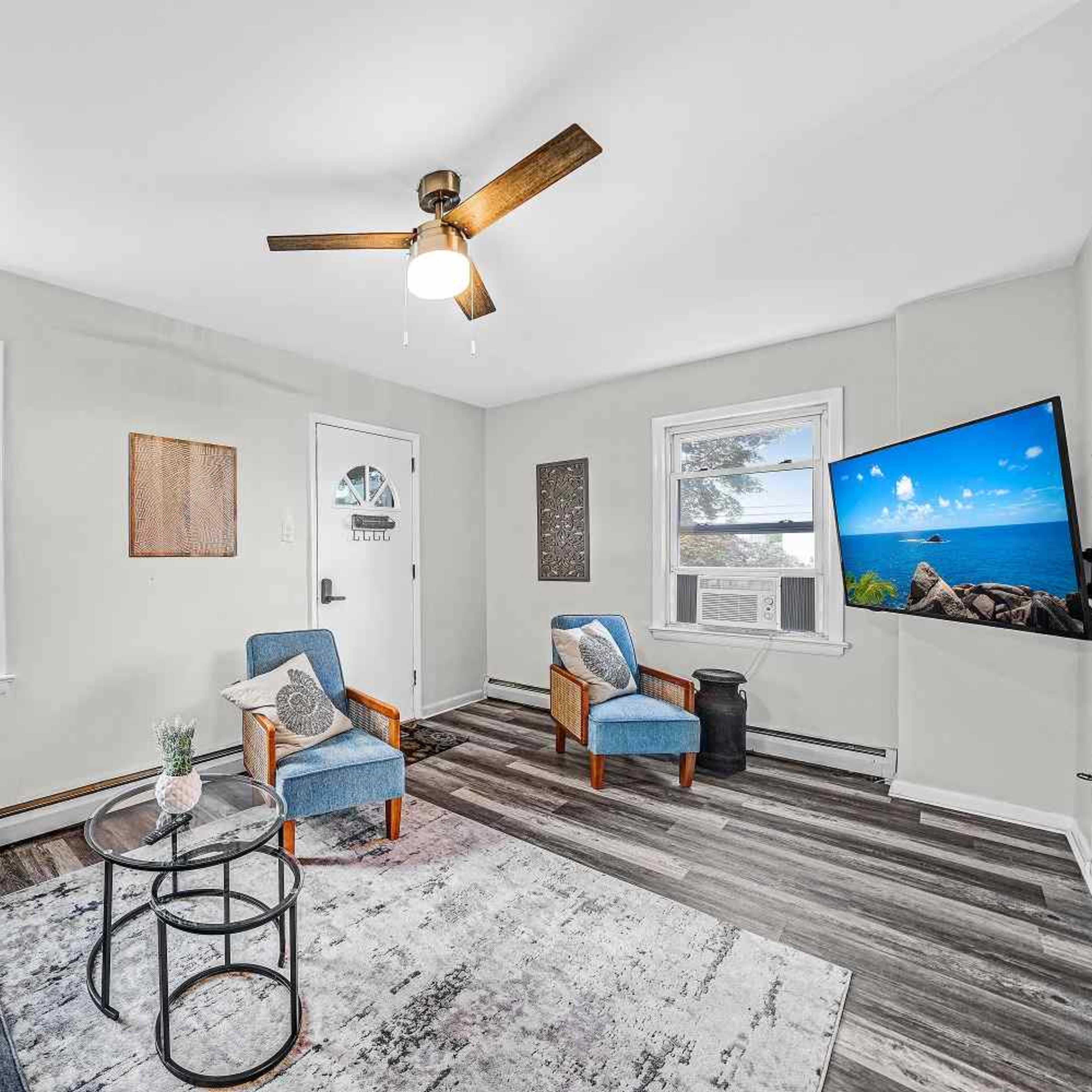 A living room with a light green wall, two blue chairs, a gray sofa, a coffee table, and a wall-mounted television.