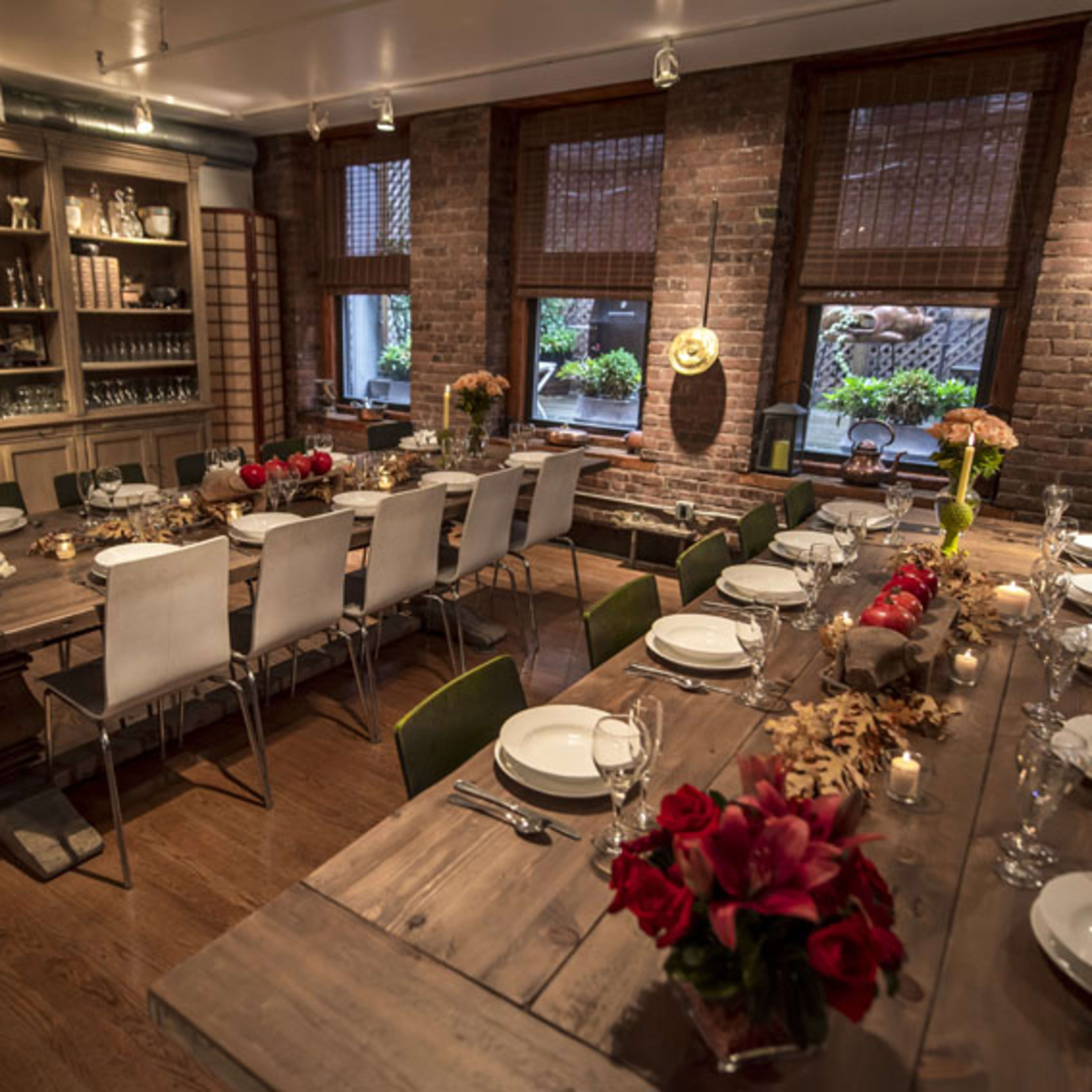 A dining room with a long wooden table set for a meal, surrounded by chairs and decorated with flowers and candles.