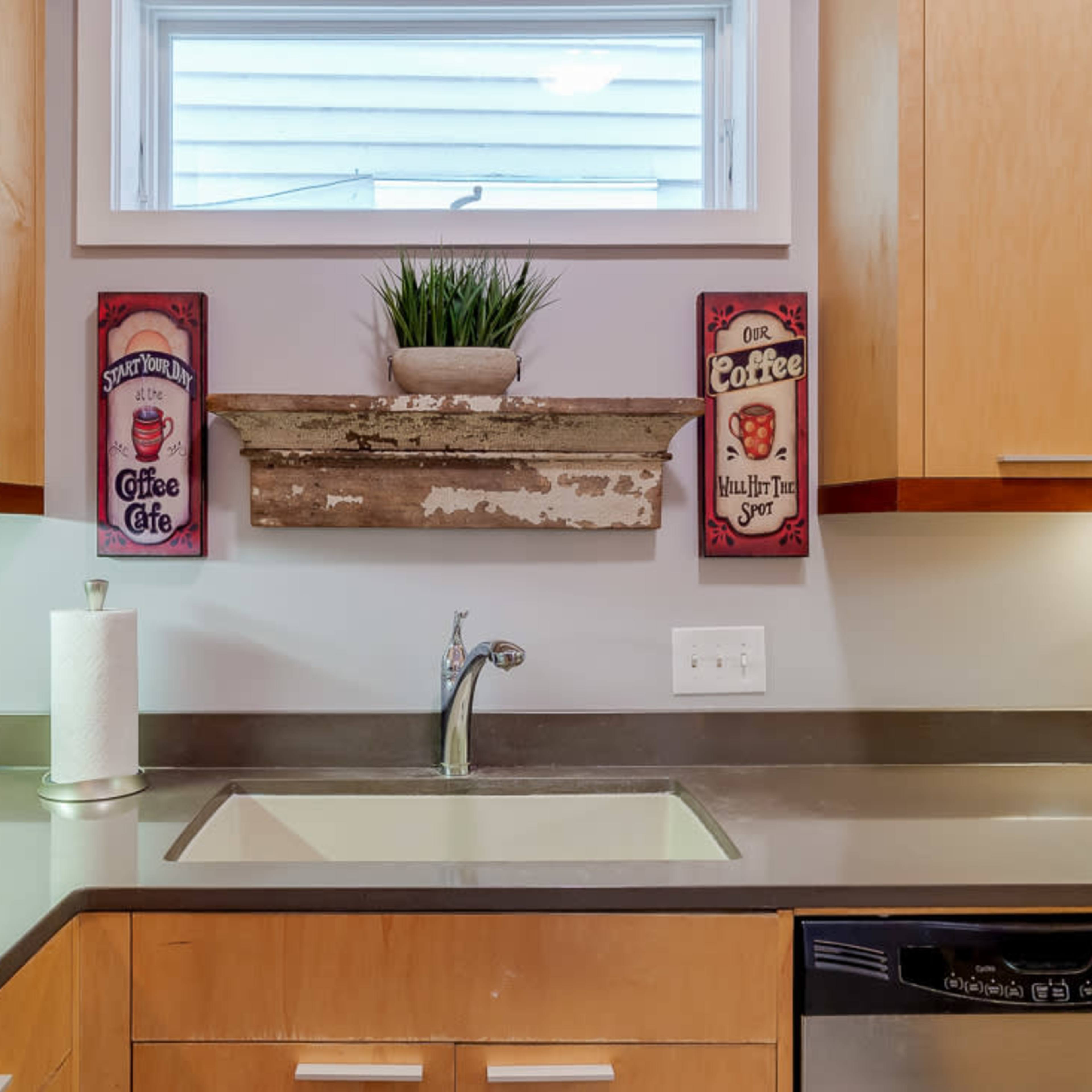 A kitchen sink area with wooden cabinets, a countertop, and decorative coffee-themed signs on the wall above.