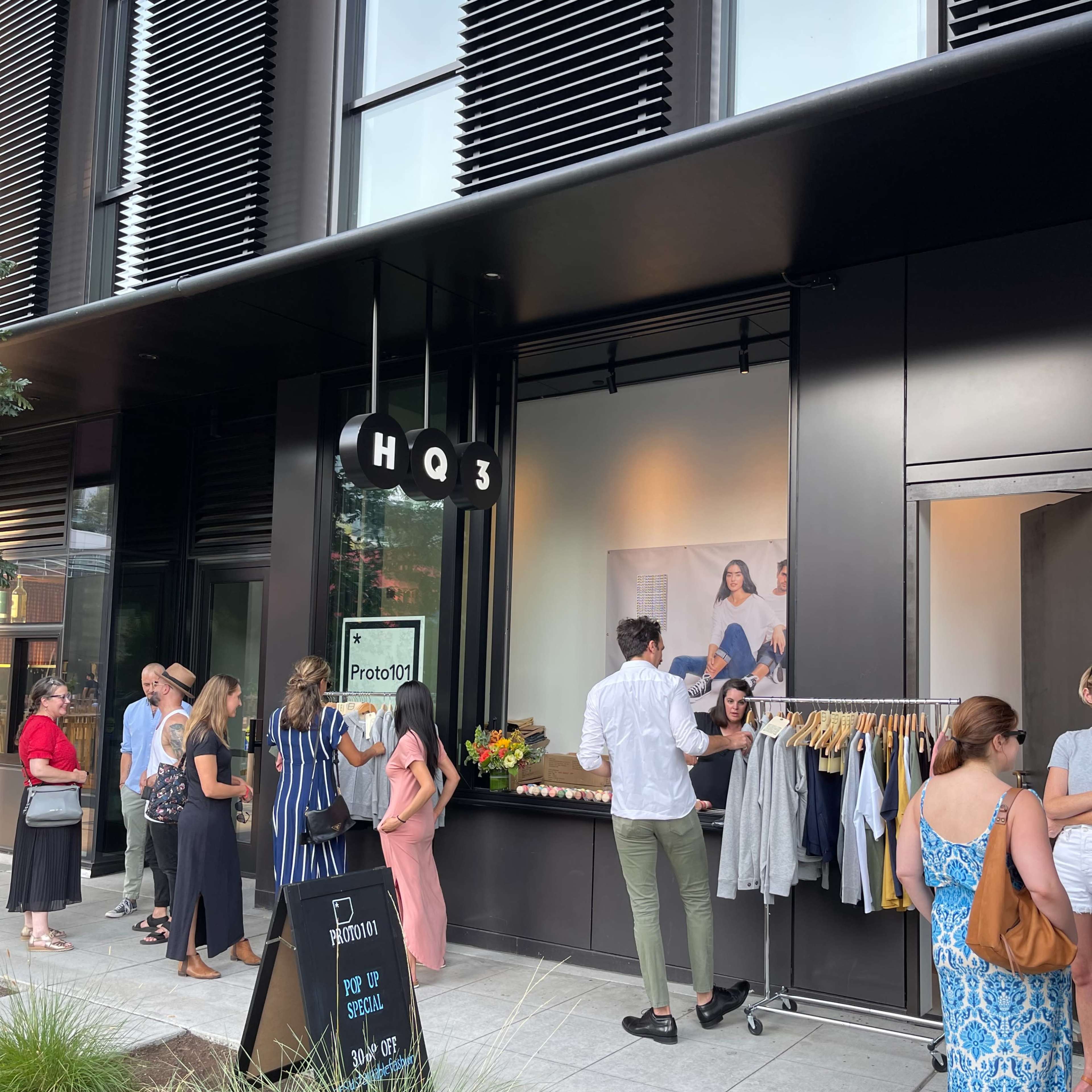 A crowd of people gathers outside a modern retail space featuring a display of clothing and a promotional sign.