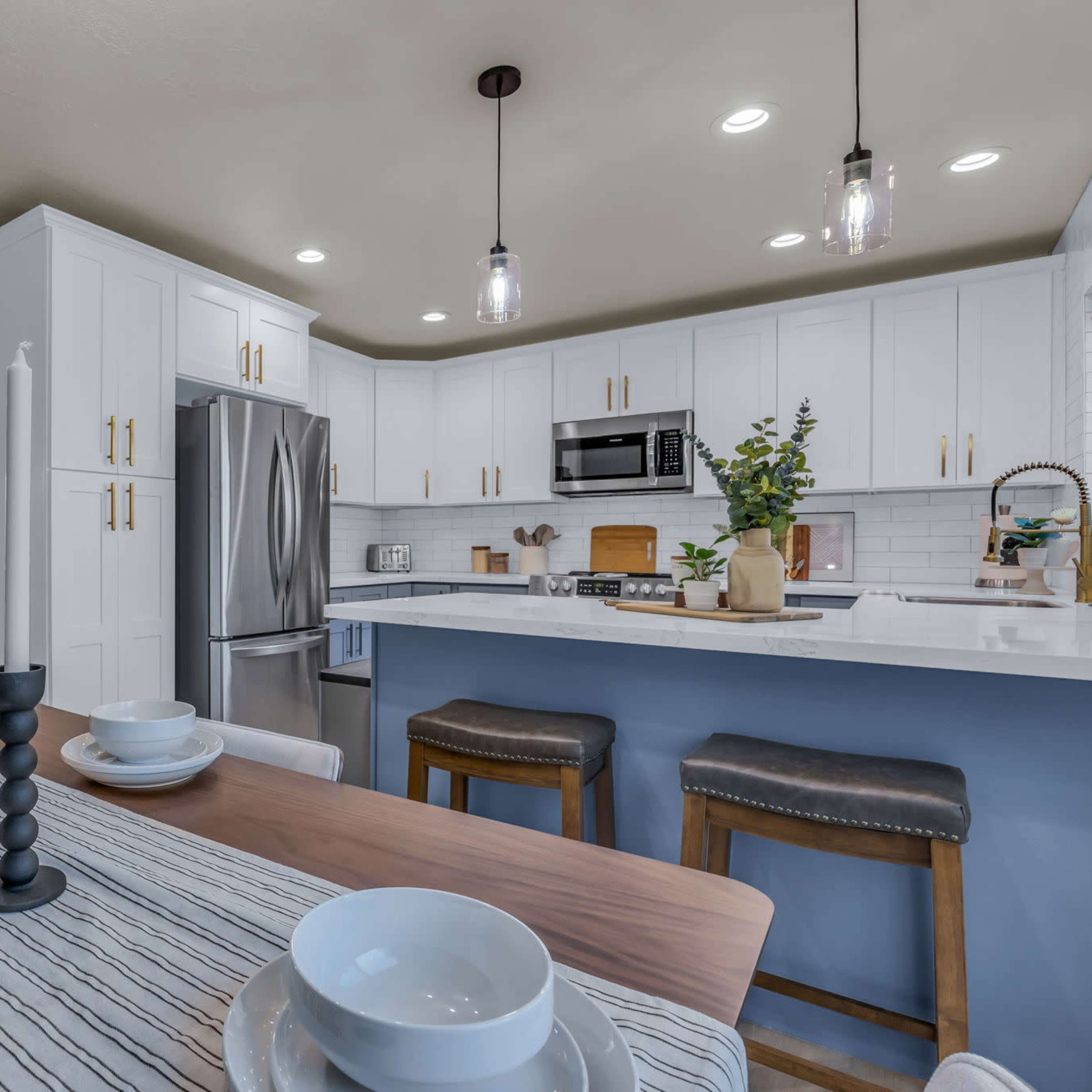 A modern kitchen features white cabinetry, stainless steel appliances, and a dining table set with dishes and candlesticks.