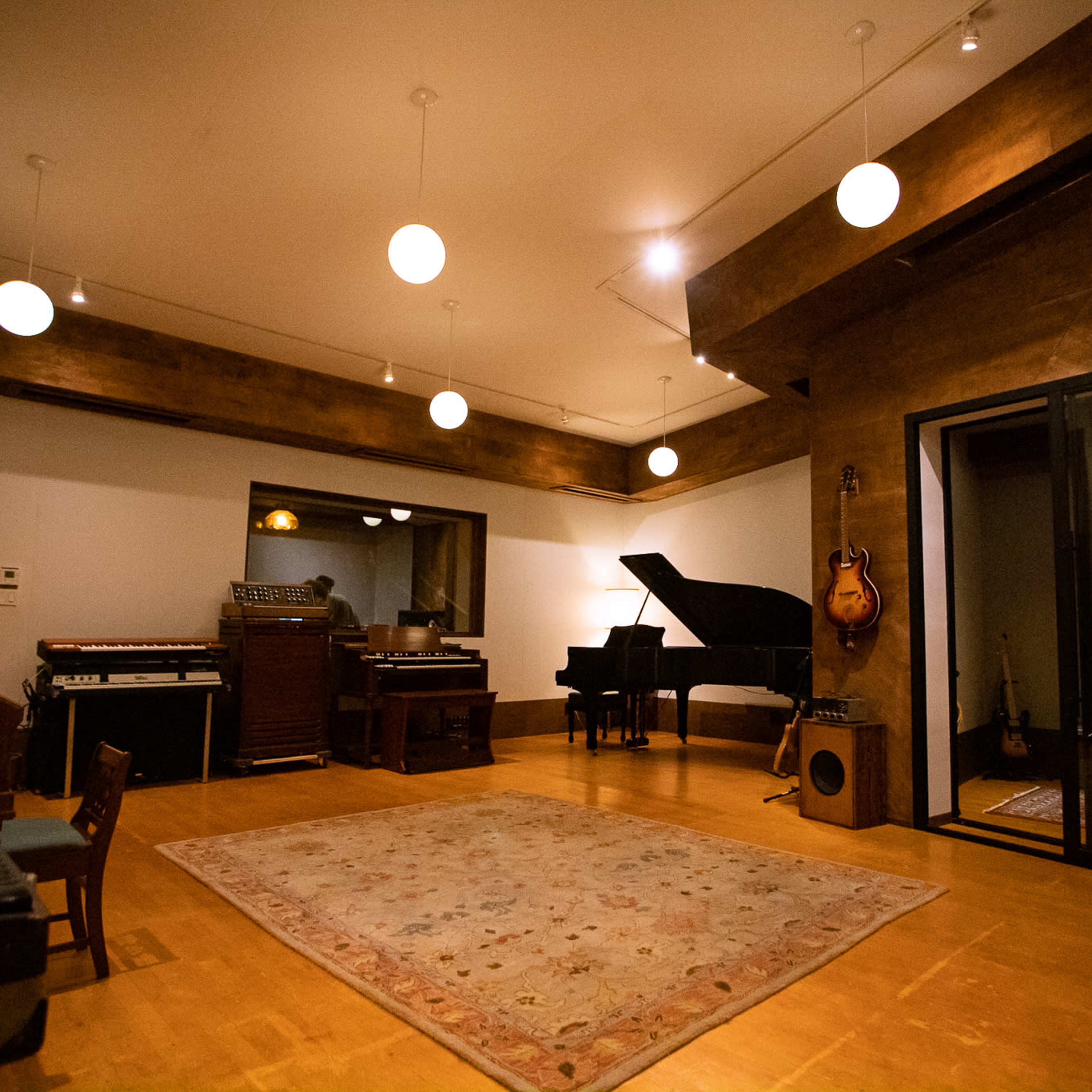A spacious music studio with a grand piano, an electric guitar on a stand, and various instruments arranged around a large area rug.