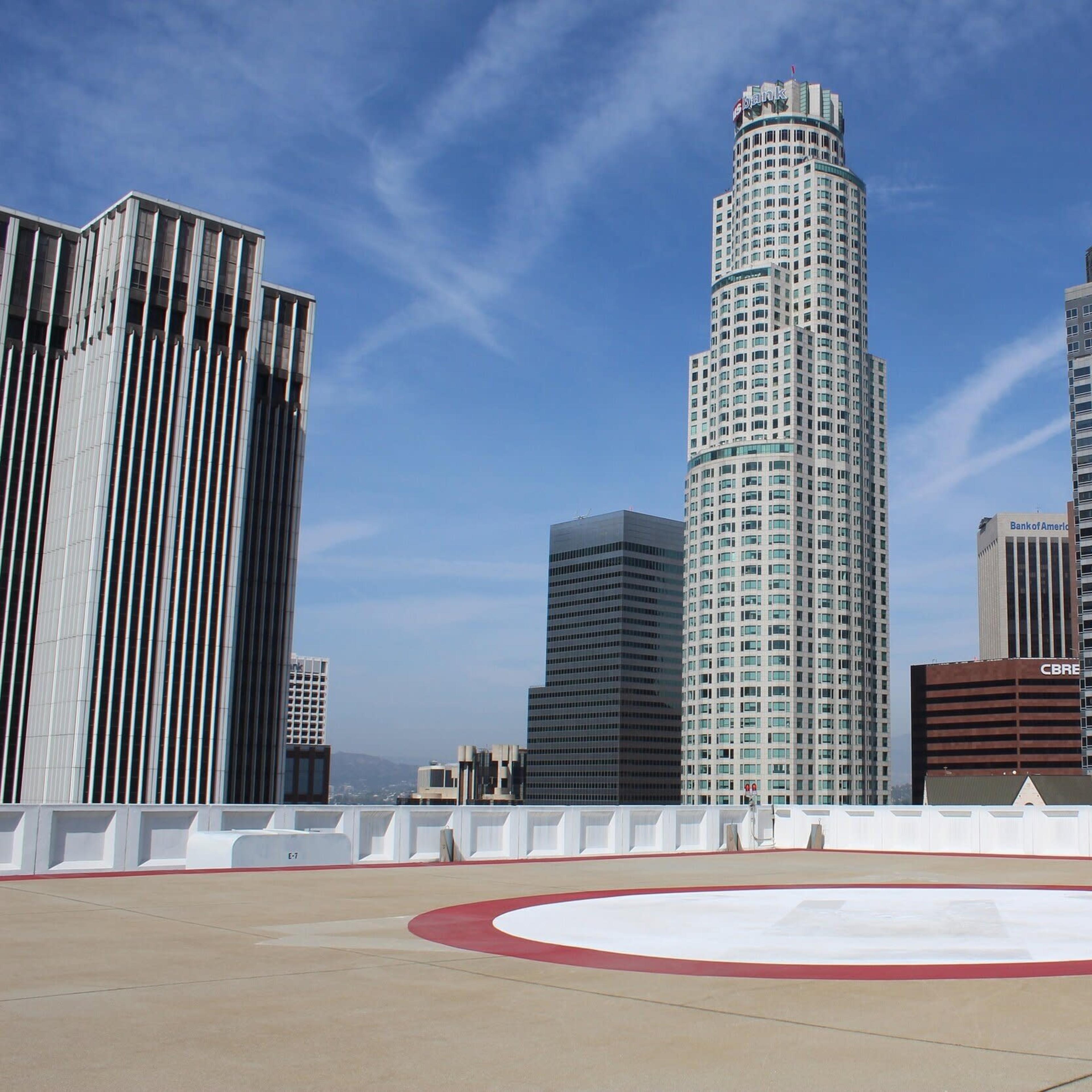 A rooftop helipad surrounded by several high-rise buildings in an urban skyline against a blue sky.