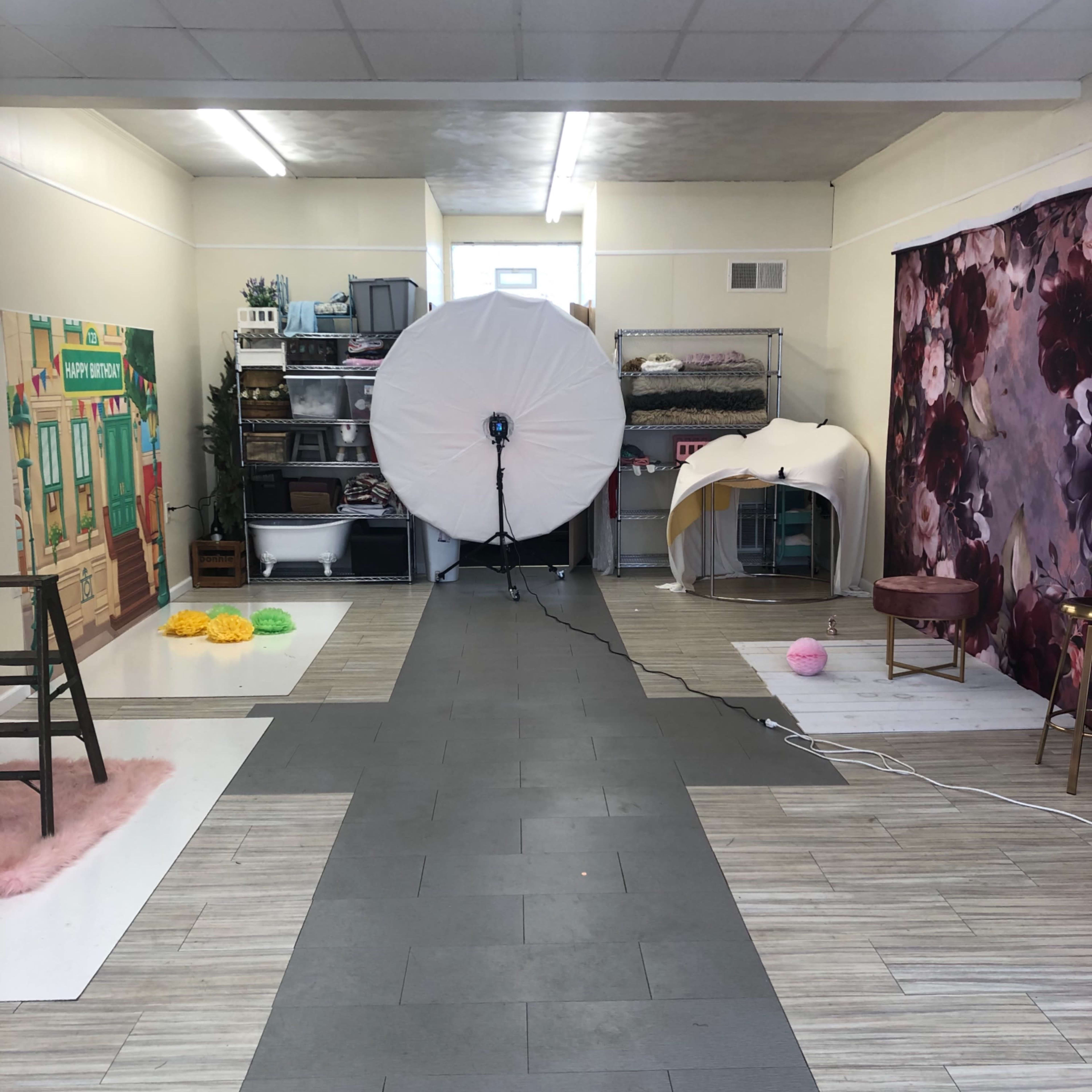 A photography studio with a large light setup at the center, surrounded by various props and backdrops.