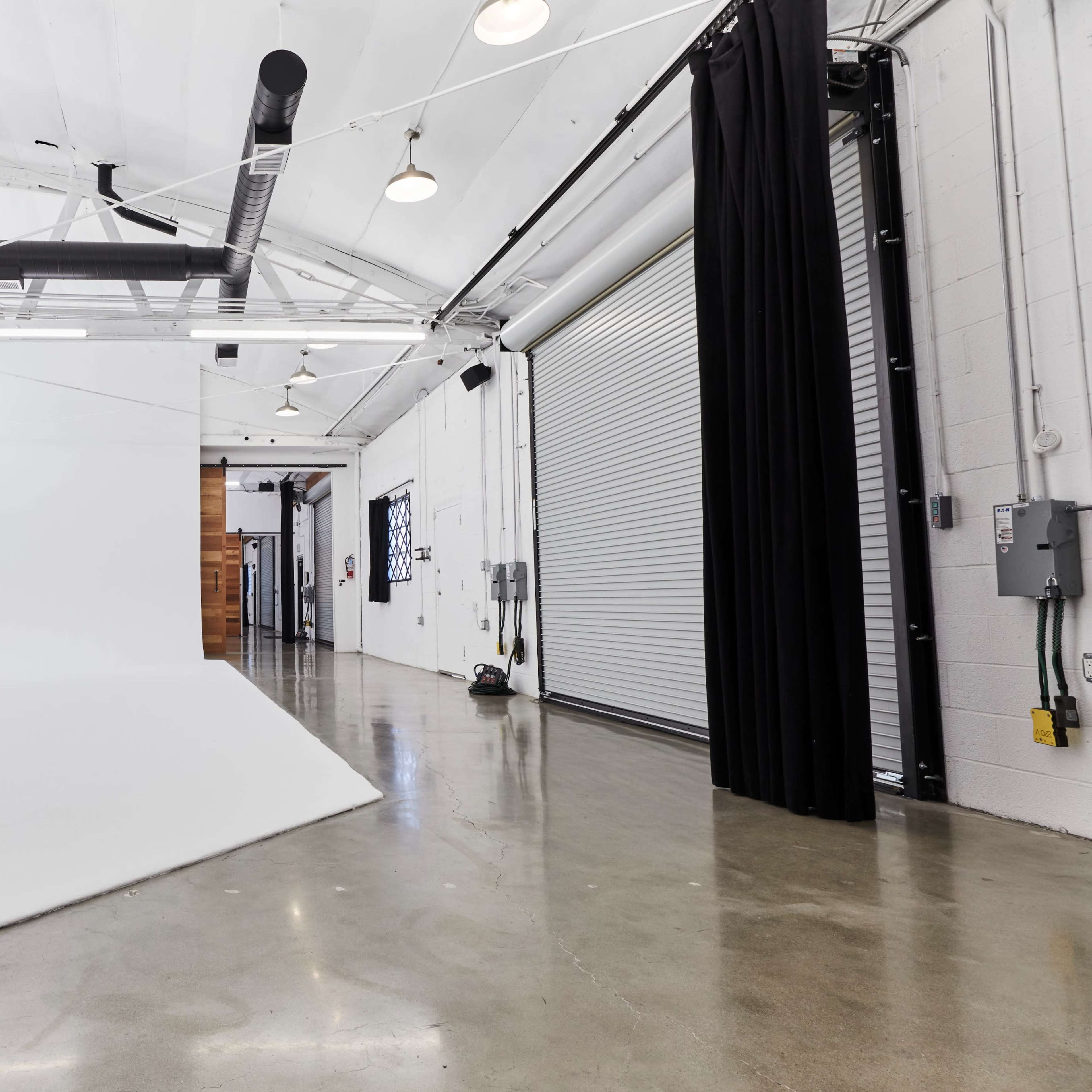 A spacious interior of a studio with white walls, a polished concrete floor, and a large roll-up door on one side.