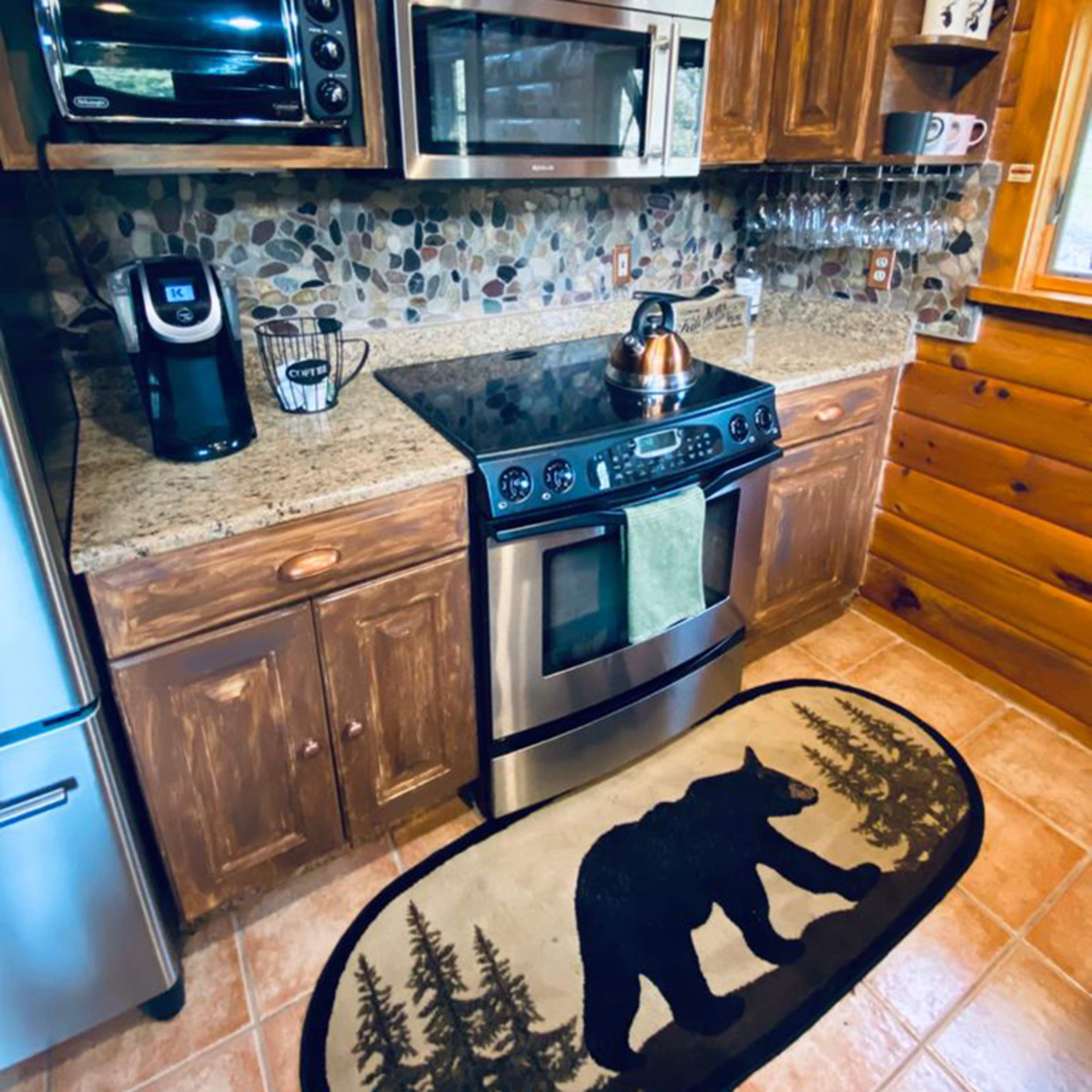 A rustic kitchen with wooden cabinets, stainless steel appliances, and a bear-themed rug in front of the stove.
