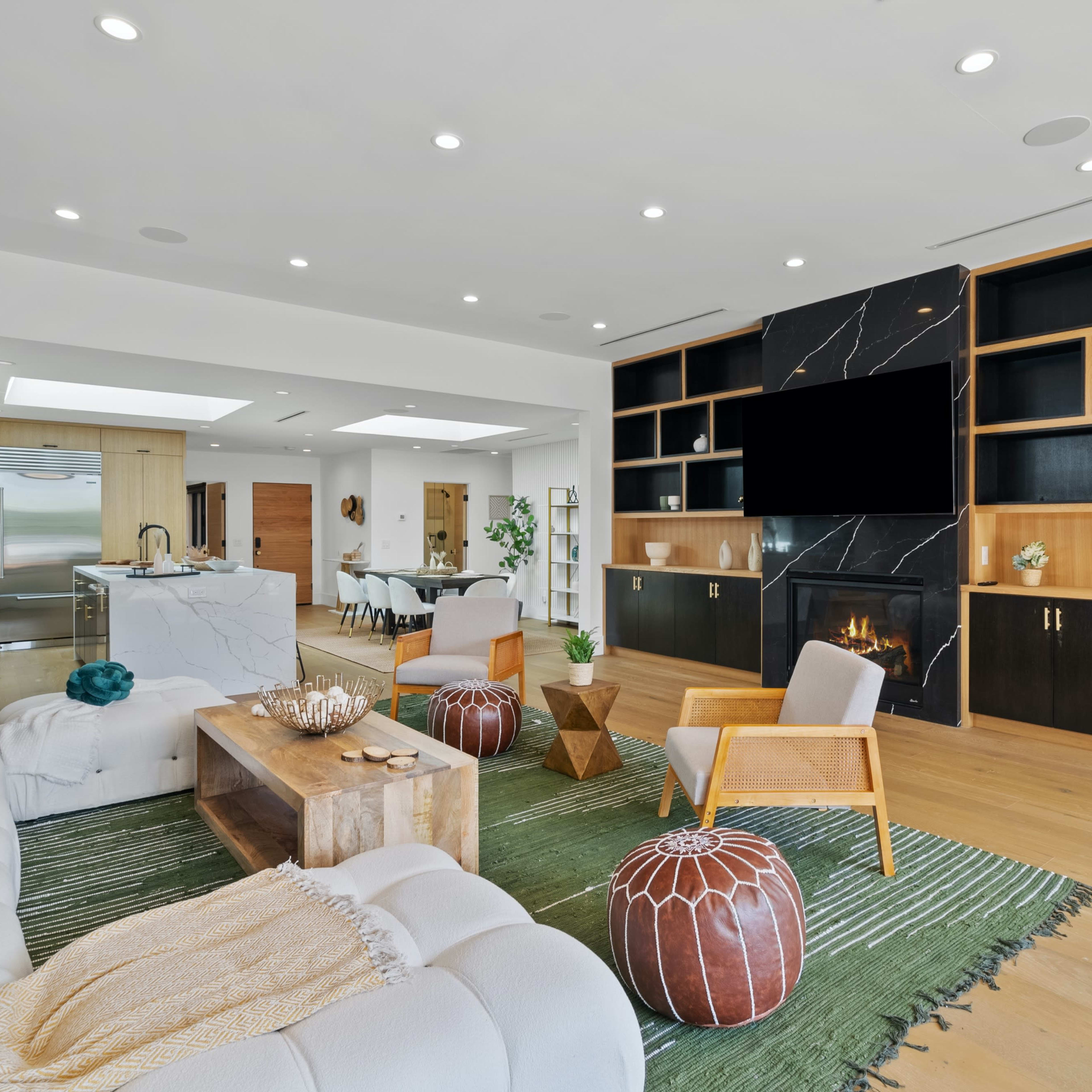 The room features a modern living area with a white sectional sofa, wooden coffee table, and a black marble media wall with a fireplace, surrounded by shelves and a green area rug.