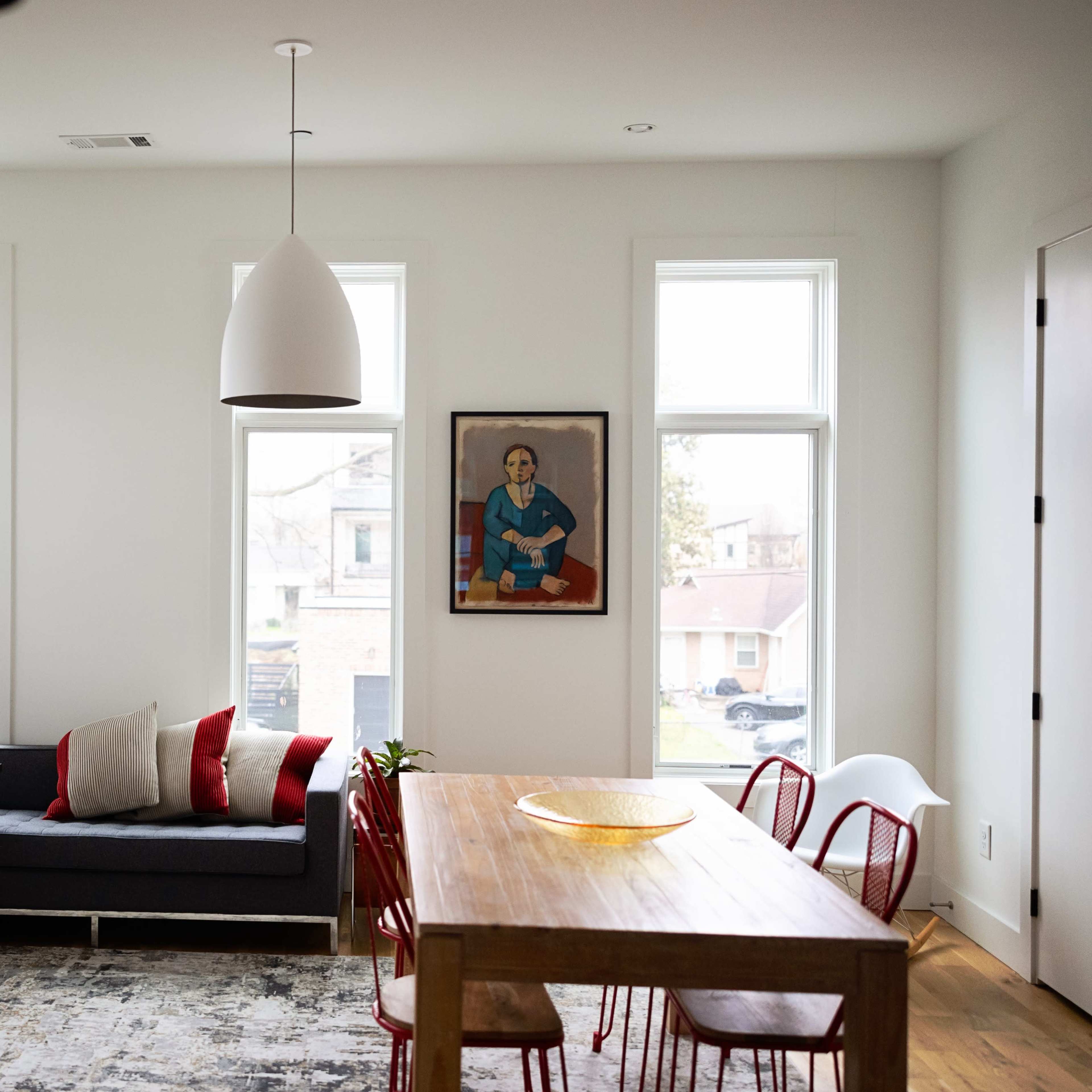 A modern living room with a sectional sofa, a wooden dining table surrounded by red chairs, and a framed artwork on the wall.