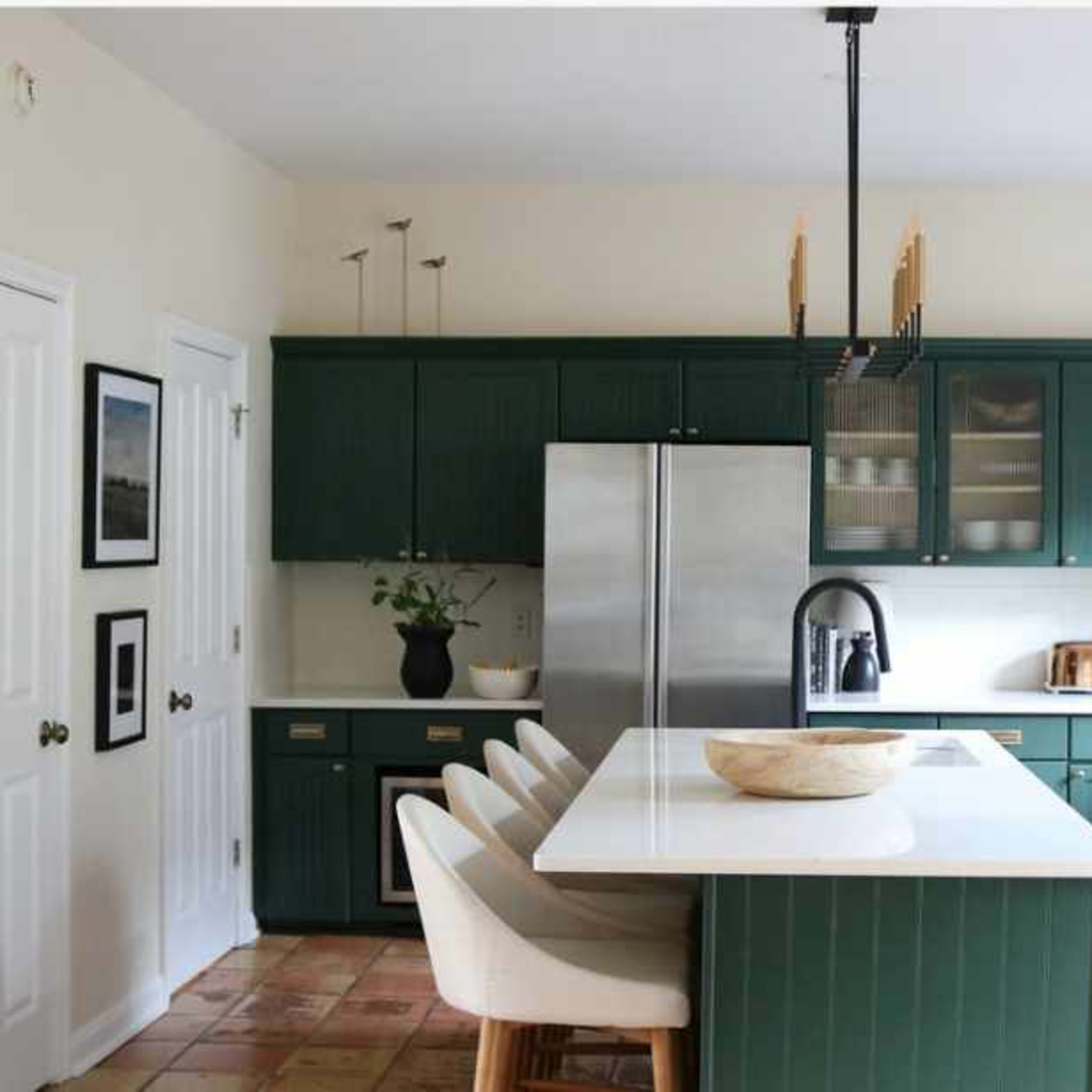 A modern kitchen features green cabinetry, a central island with seating, stainless steel appliances, and natural light streaming in from a window.